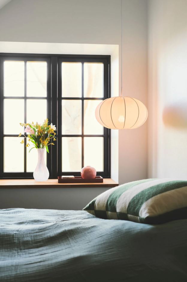 Bedroom with a window, pendant light, and vase of flowers.