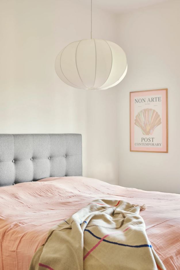 Bedroom with pink bedding and a white pendant light hanging above.