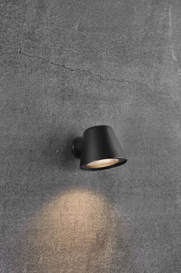A black outdoor wall-mounted light with a directional beam, installed on a grey textured wall.