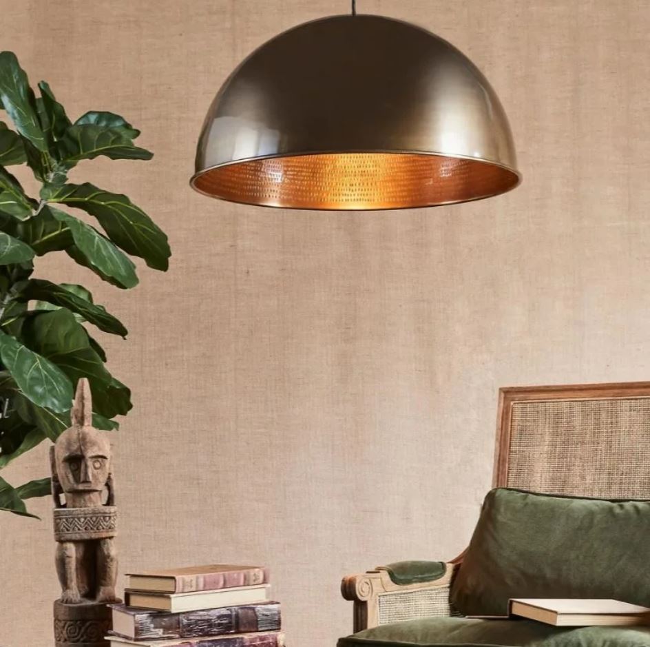 A modern industrial pendant light with a brass metal dome, featuring a matte black exterior and a polished silver interior, suspended above a living room setting.