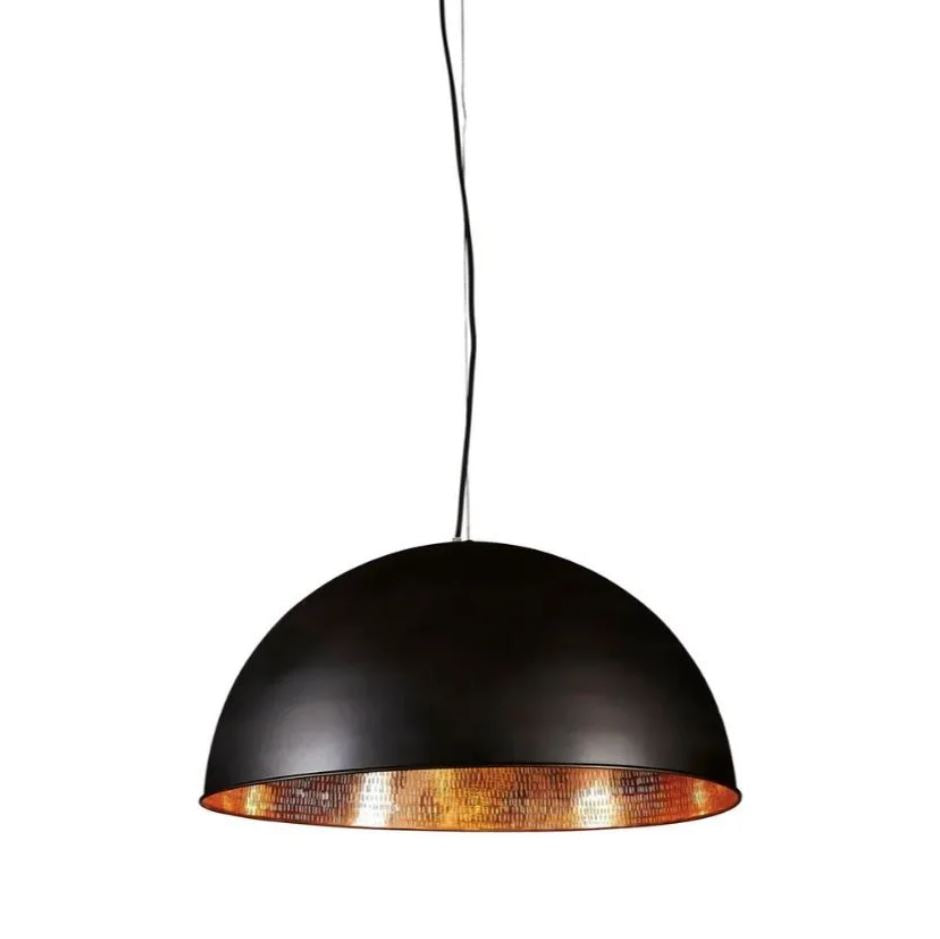 A modern industrial pendant light with a brass metal dome, featuring a matte black exterior and a polished silver interior, suspended above a living room setting.