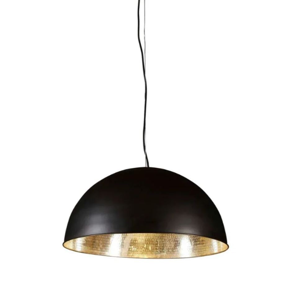 A modern industrial pendant light with a brass metal dome, featuring a matte black exterior and a polished silver interior, suspended above a living room setting.
