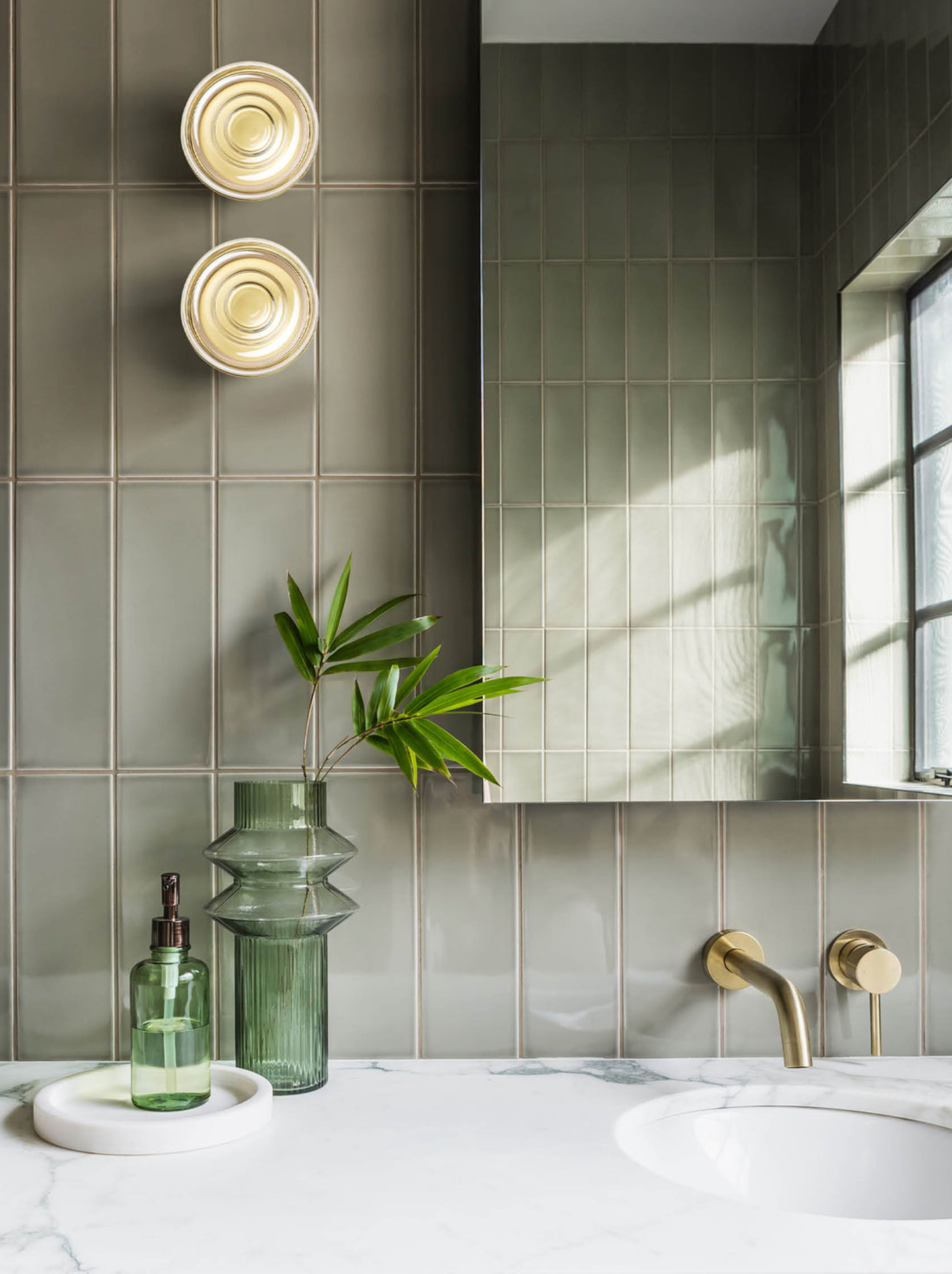 Bathroom with green tiles, a mirror, and decorative wall lights. 