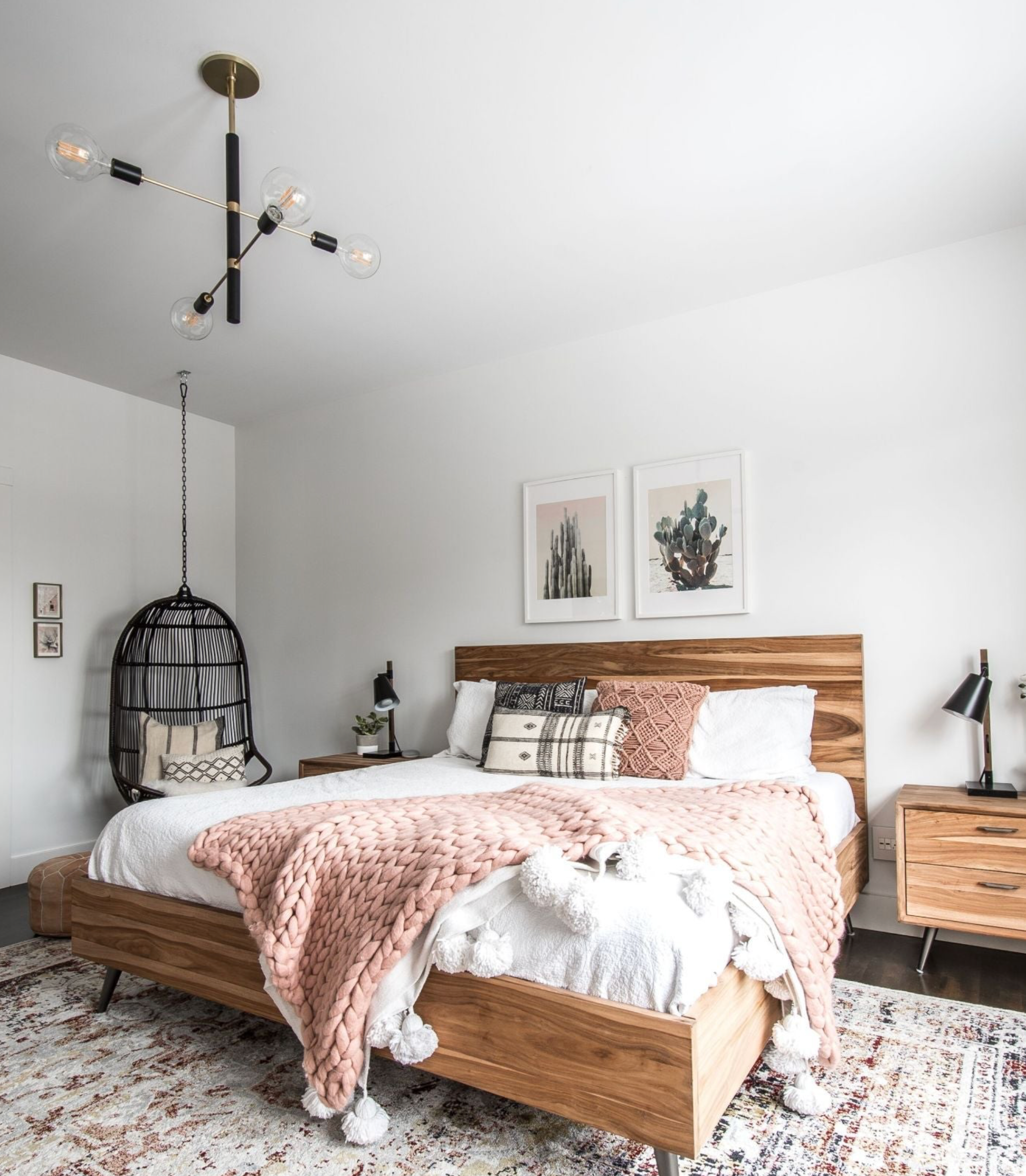 Modern bedroom with wooden bed, pink blanket, and decorative pillows and 4 globe black and brass pendant light.