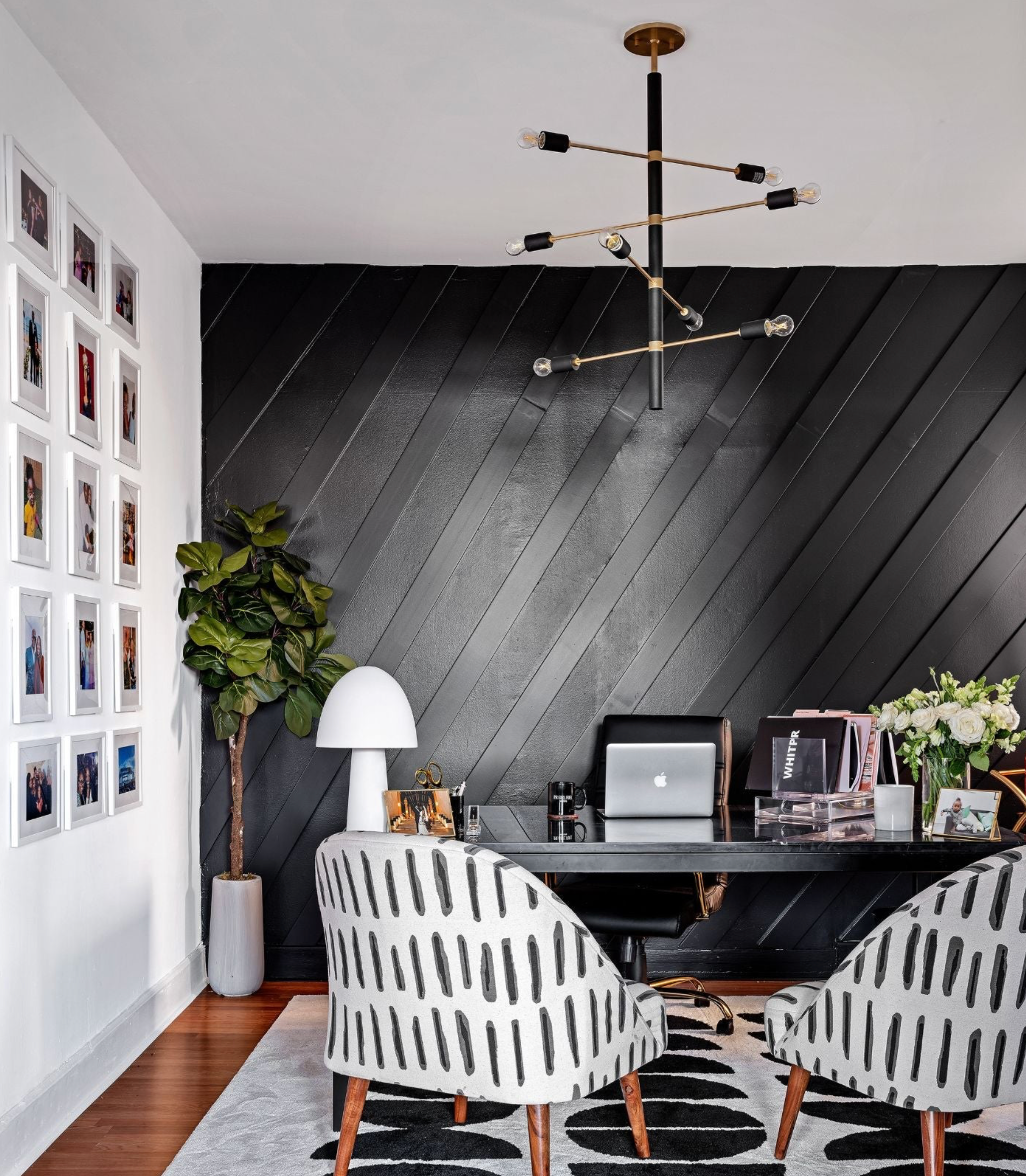Modern office with black and white decor, including a desk, chairs, and a chandelier.