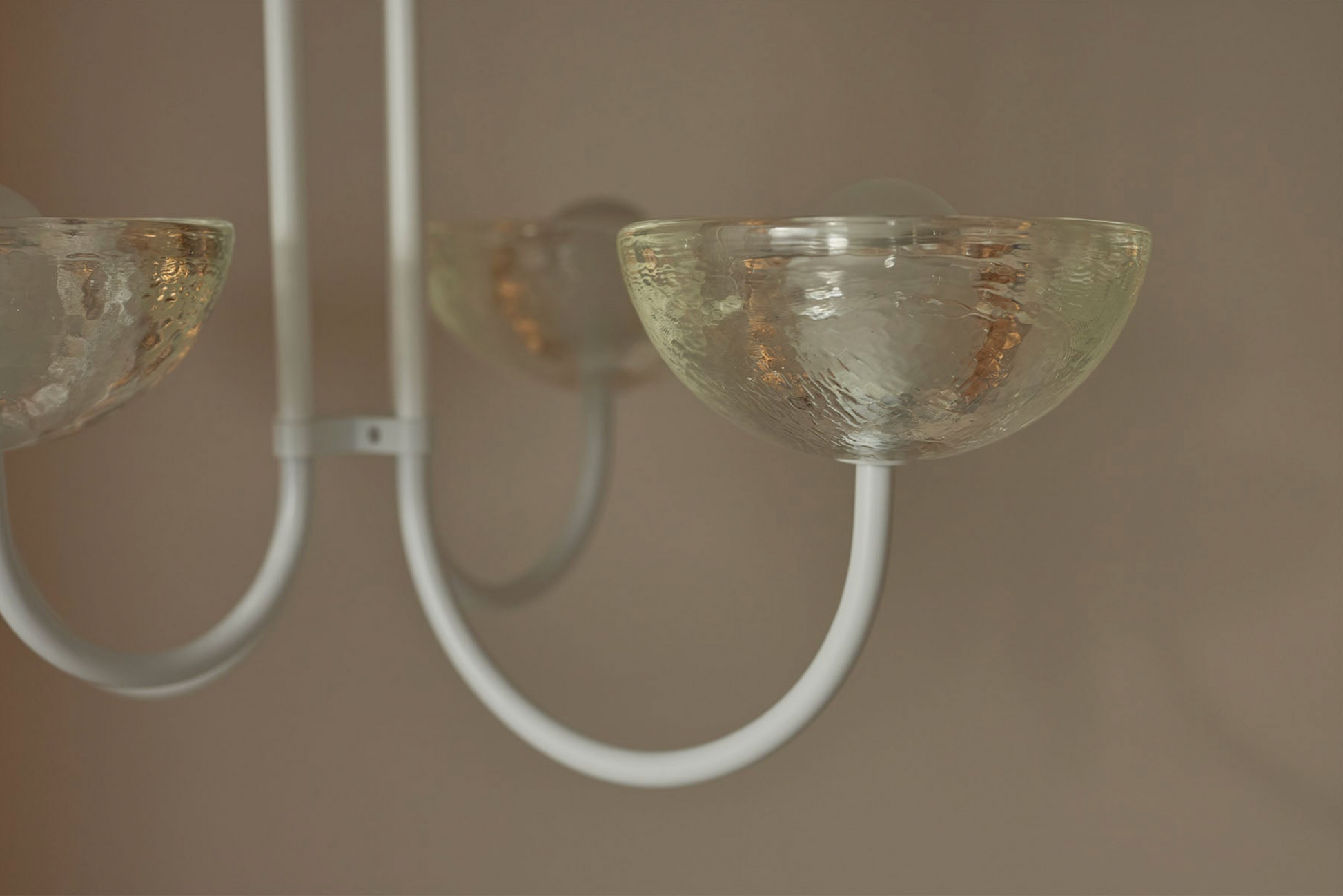 Close-up of a modern chandelier with glass shades and white metal arms against a neutral background.