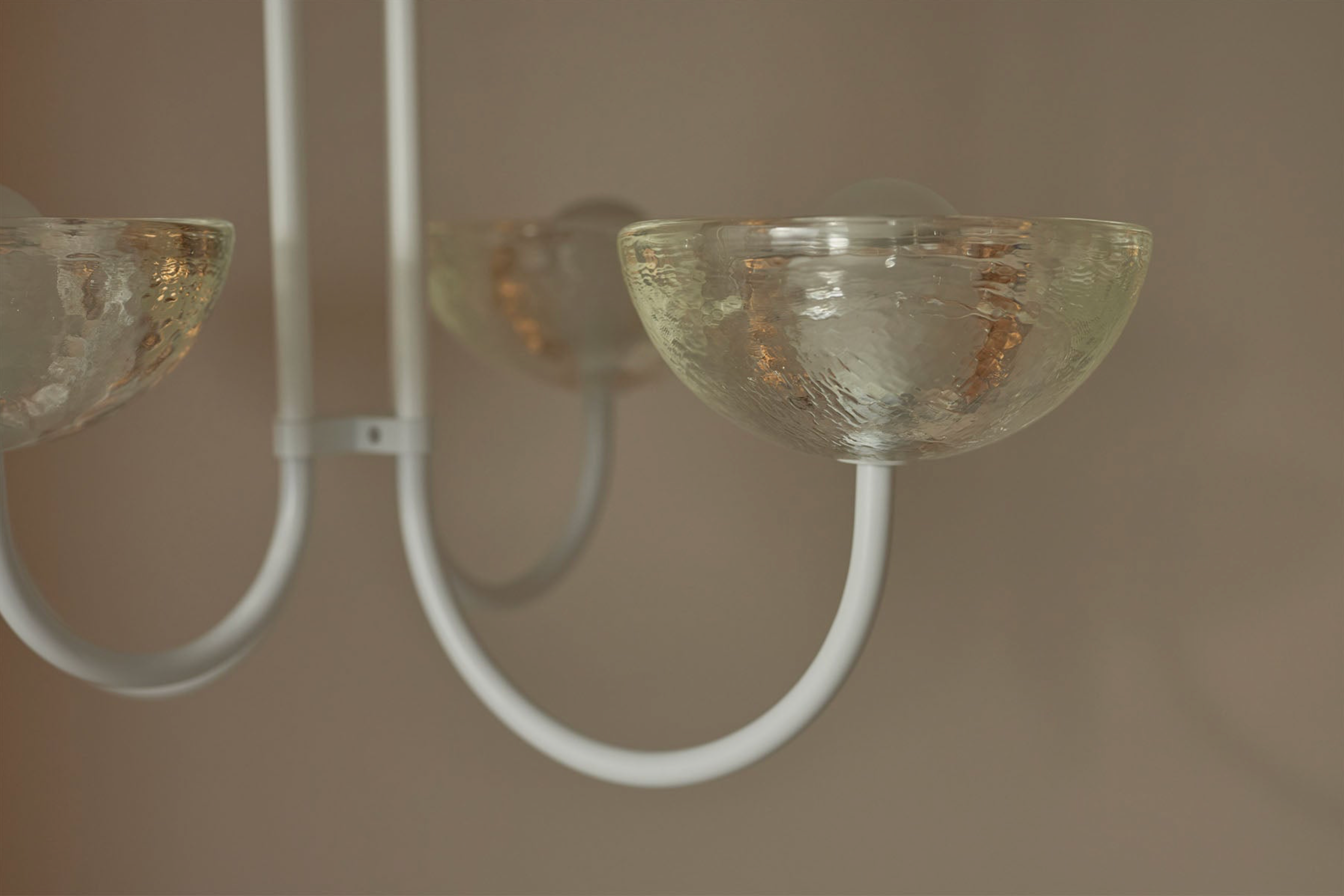 Close-up of a modern chandelier with glass shades and white metal arms against a neutral background.