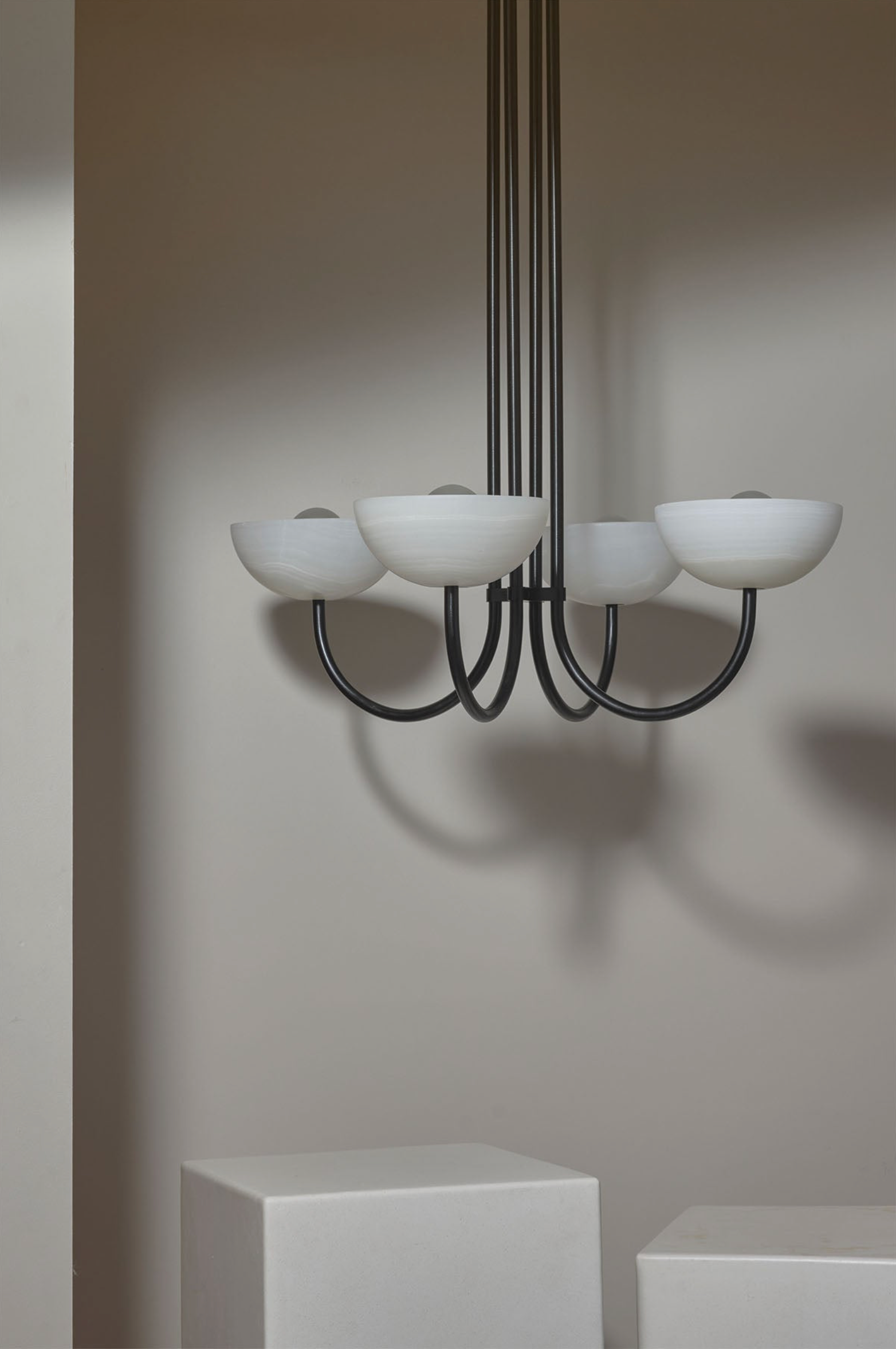 Modern chandelier with white stone shades and black metal frame against a plain wall.