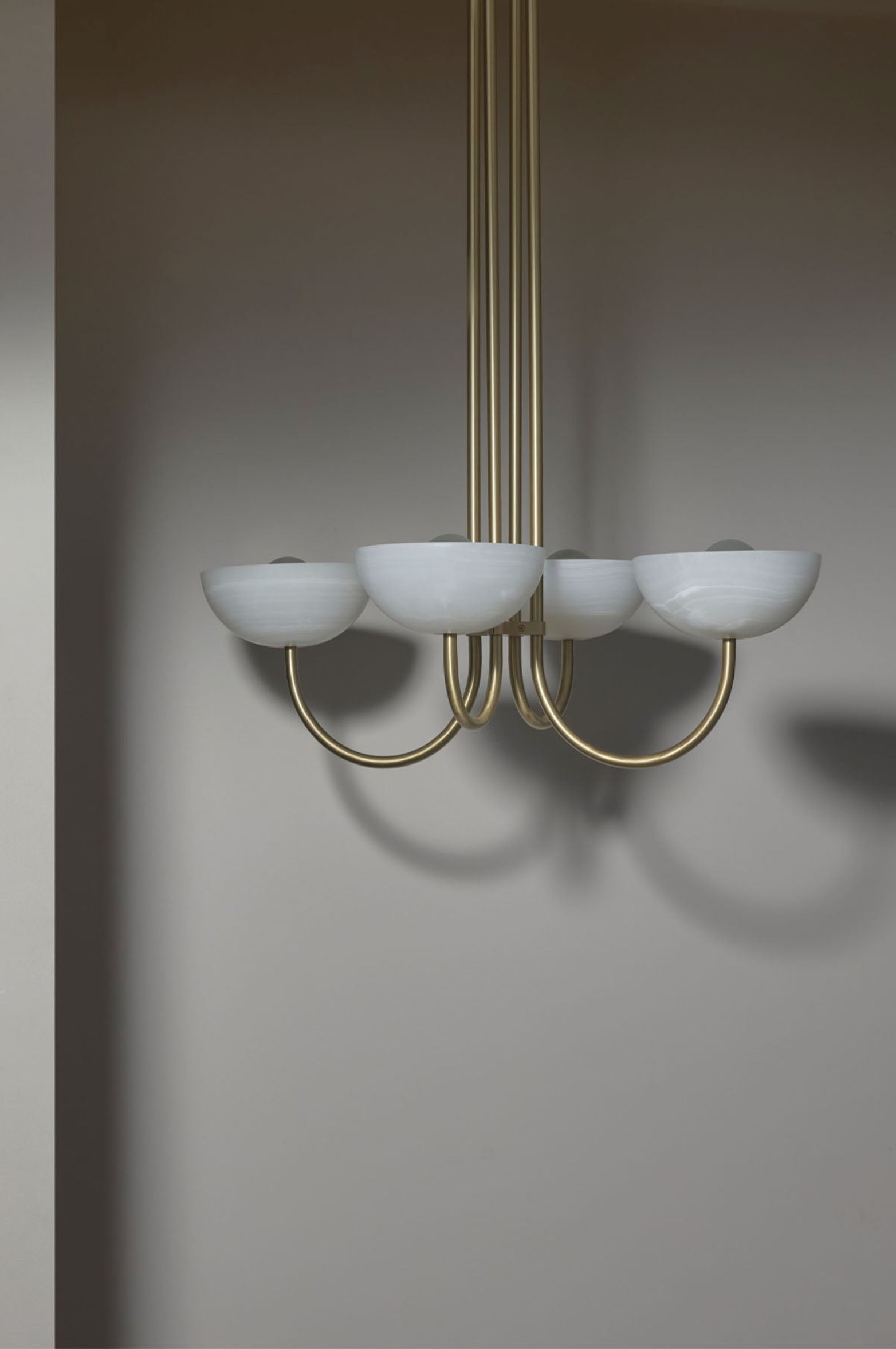 Chandelier with white stone shades and gold metal frame against a grey wall