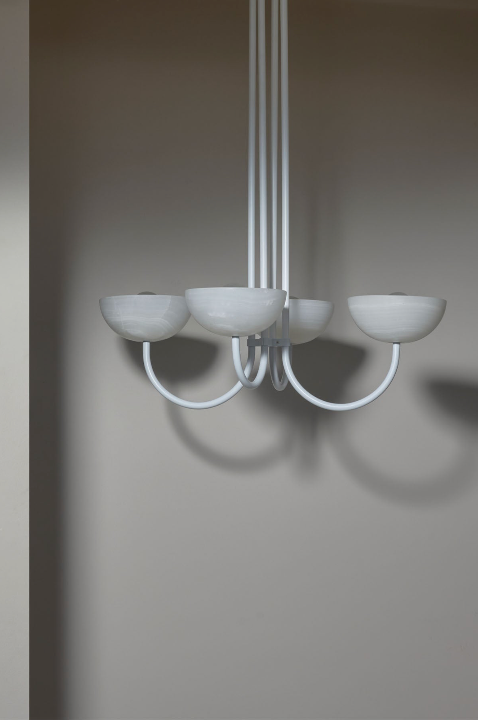 Modern chandelier with five round shades on a plain wall.