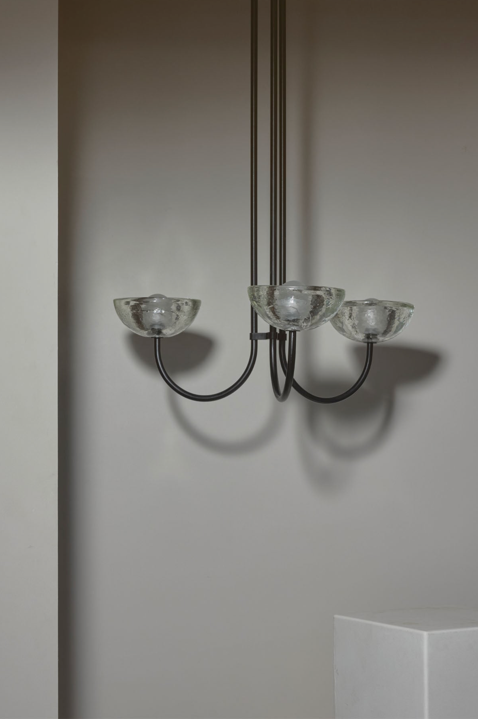 Chandelier with three glass shades on a plain wall