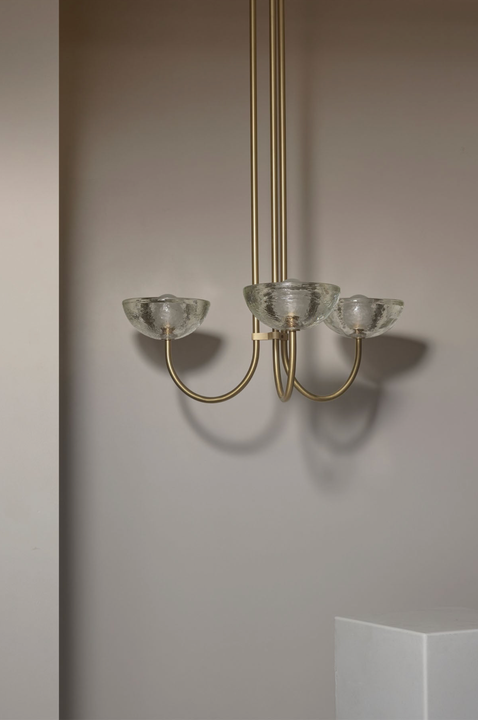 Chandelier with glass shades and gold fixture against a neutral wall.