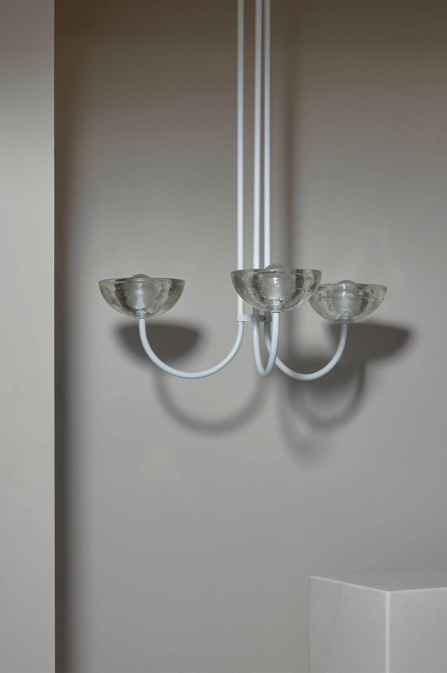 Modern chandelier with three glass shades against a plain wall.