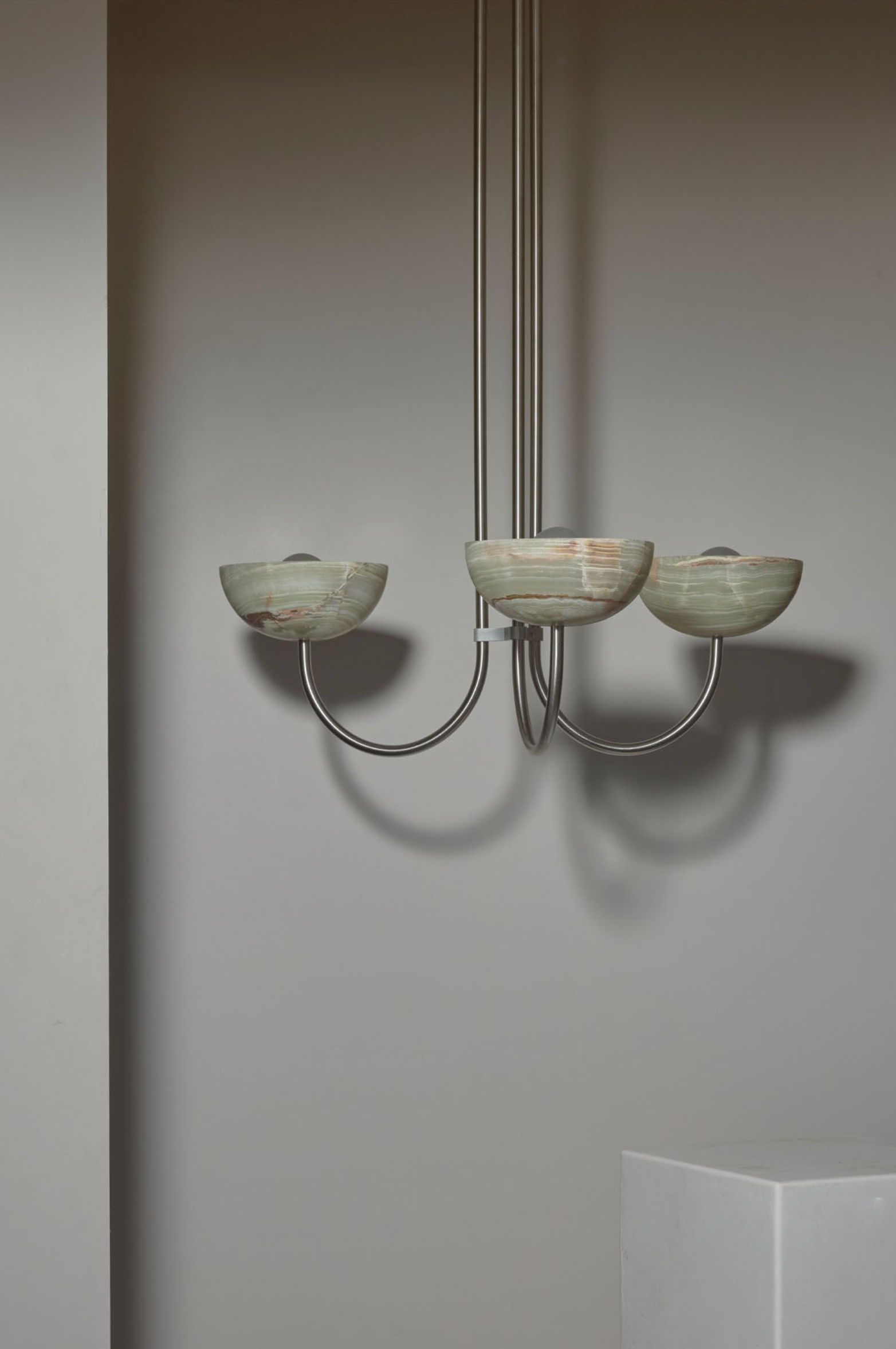 Modern chandelier with three glass shades against a plain wall.