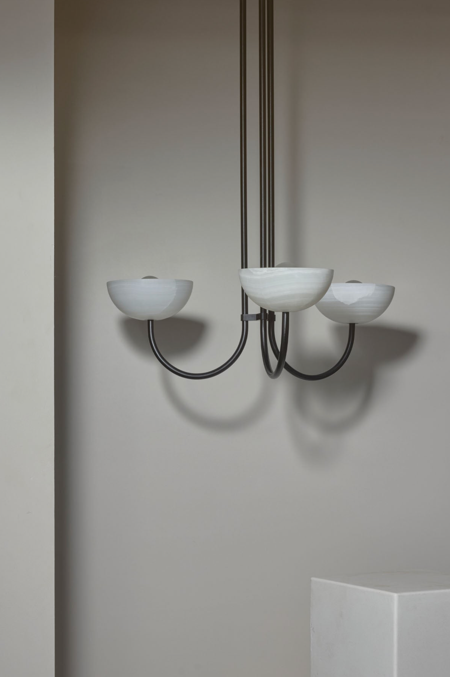 Chandelier with three white glass shades on a plain wall.