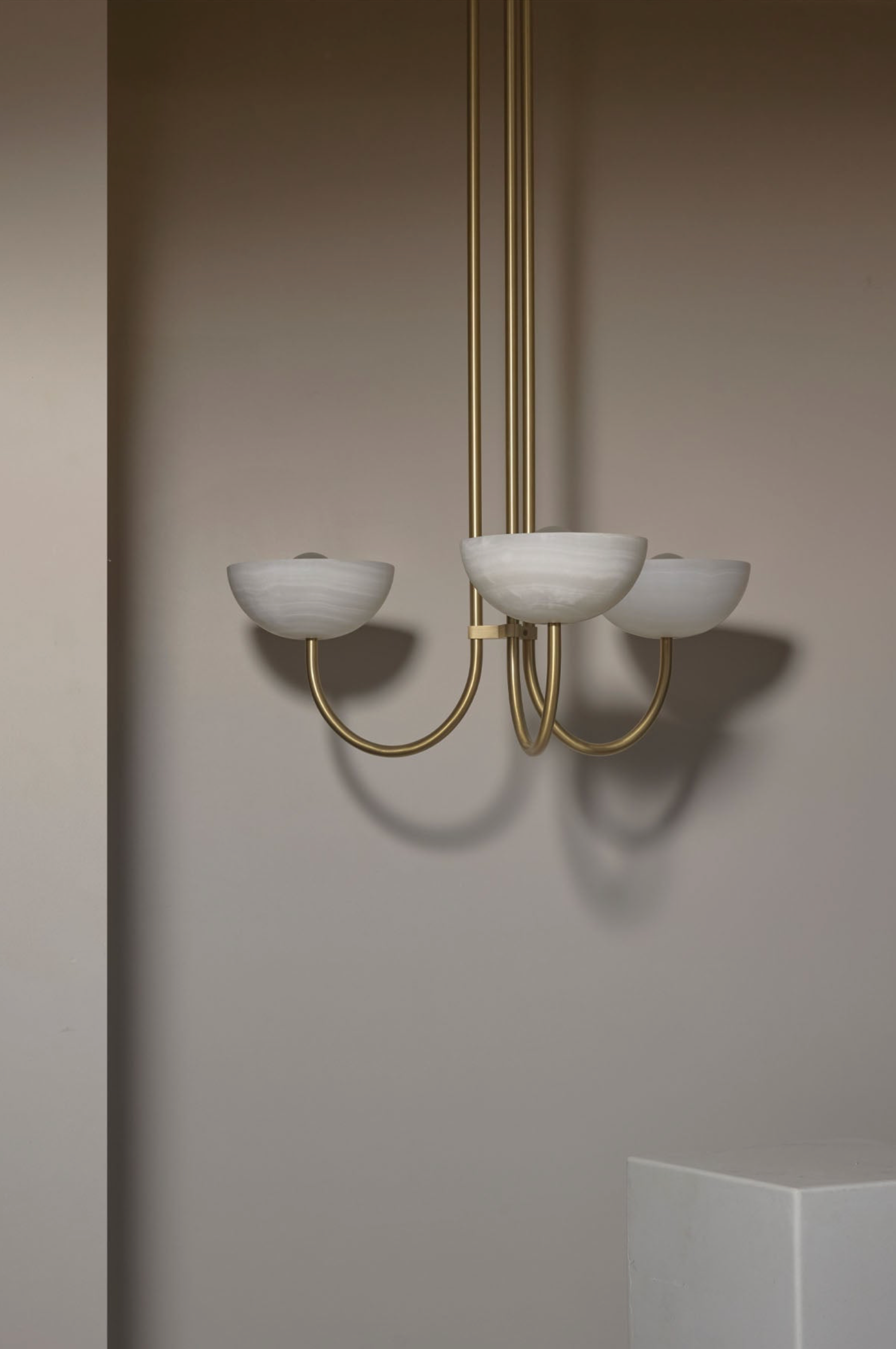 Chandelier with white glass shades and gold metal frame against a plain wall.