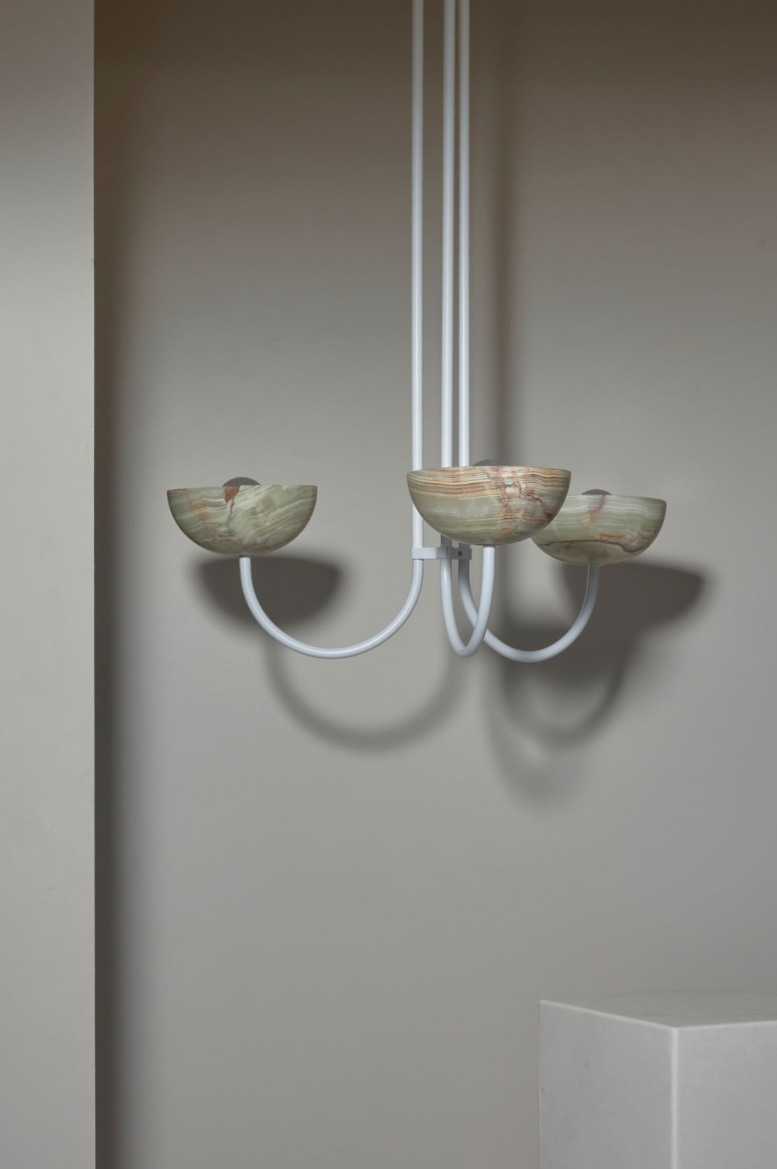 Modern chandelier with three glass shades against a plain wall.