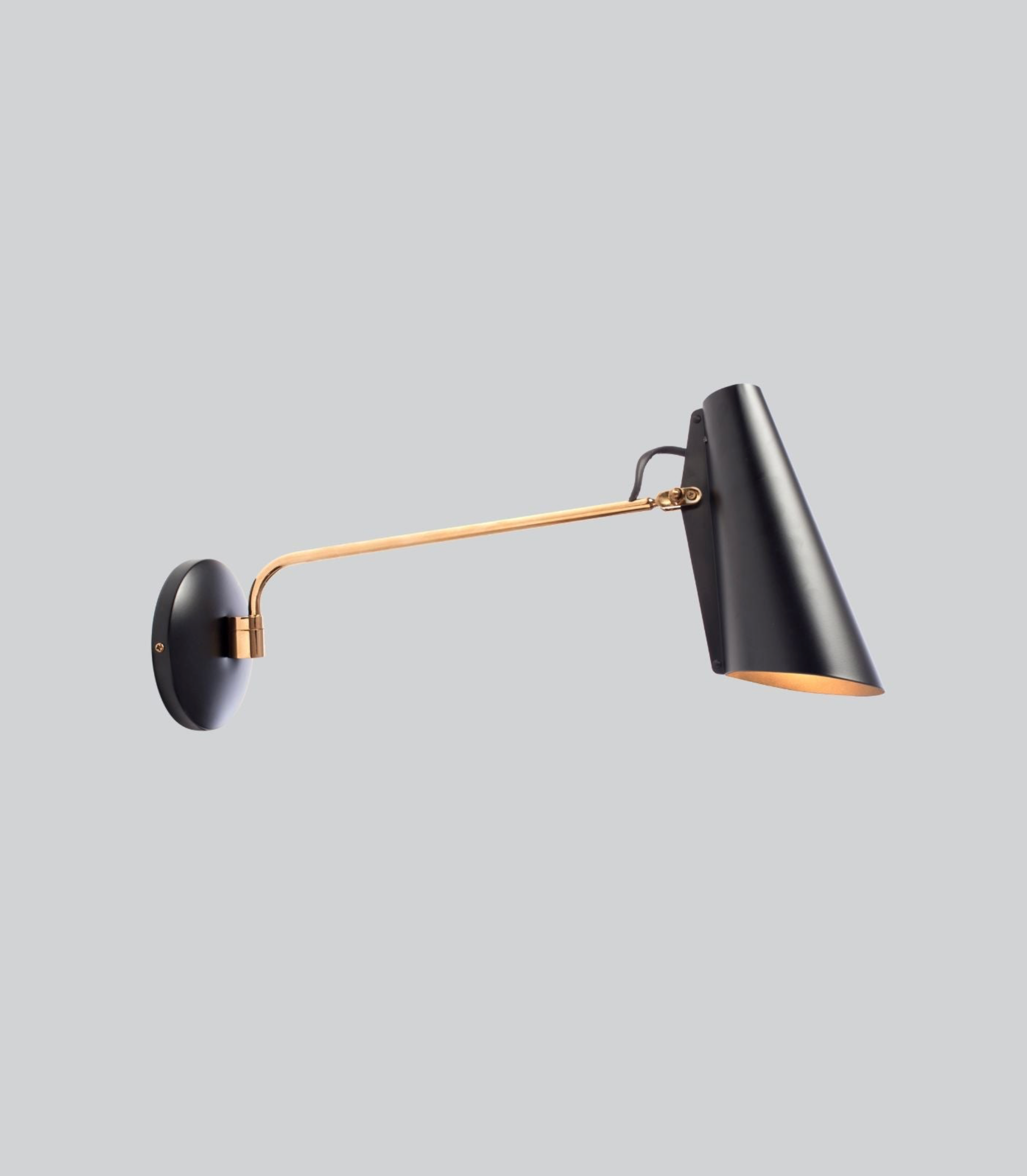 Modern wall lamp with black shade and gold arm on a light gray background