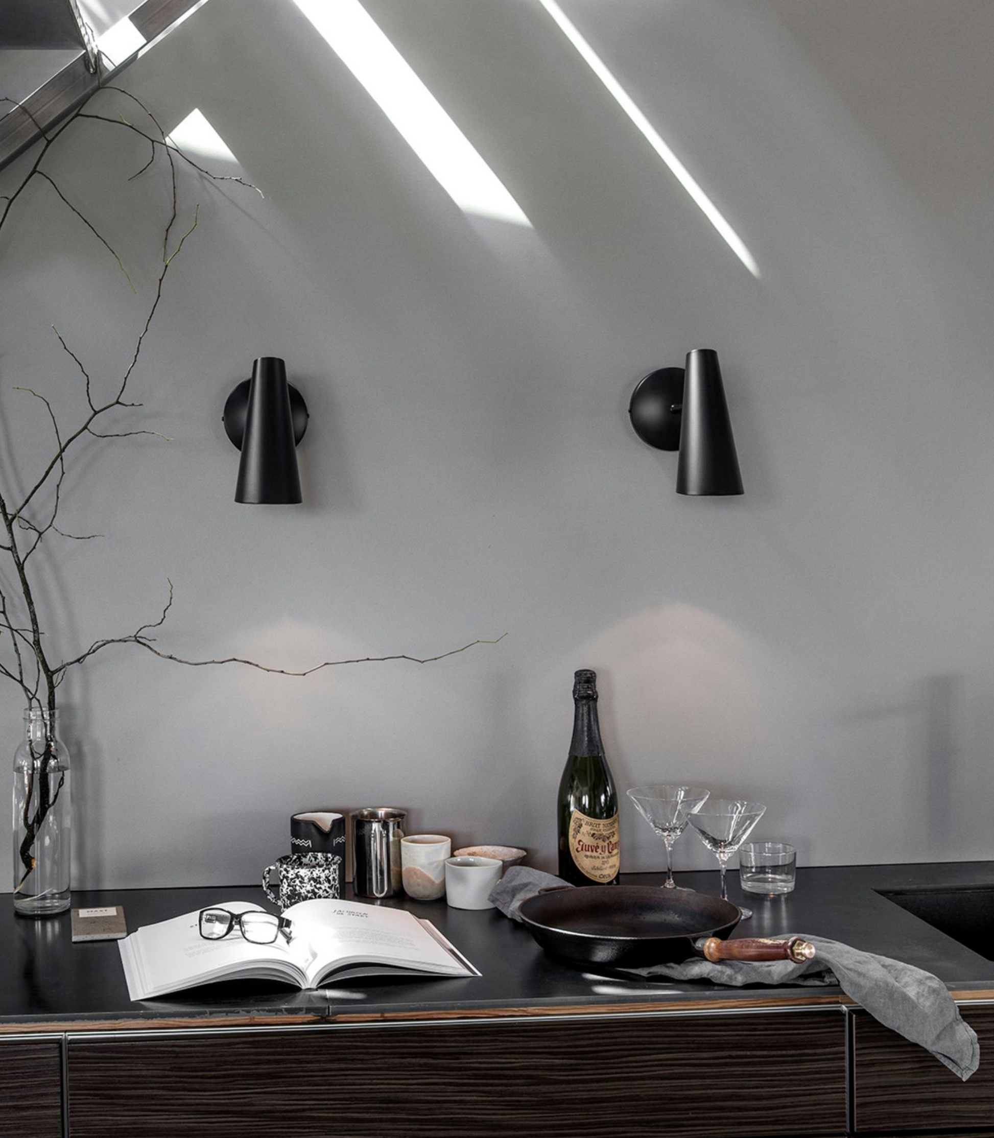 Modern kitchen counter with bottles, glasses, and an open book against a gray wall.