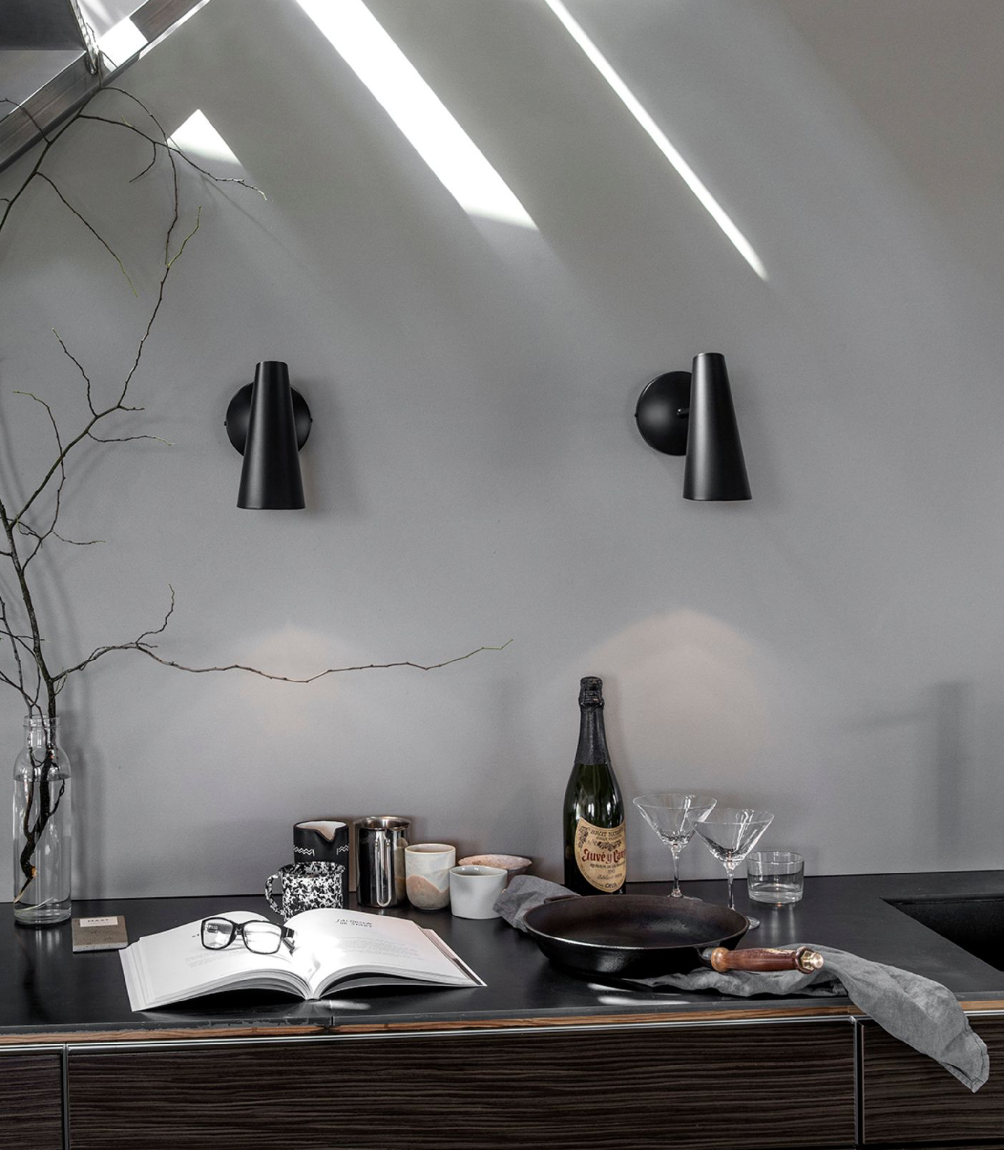 Modern kitchen counter with bottles, glasses, and an open book against a gray wall.