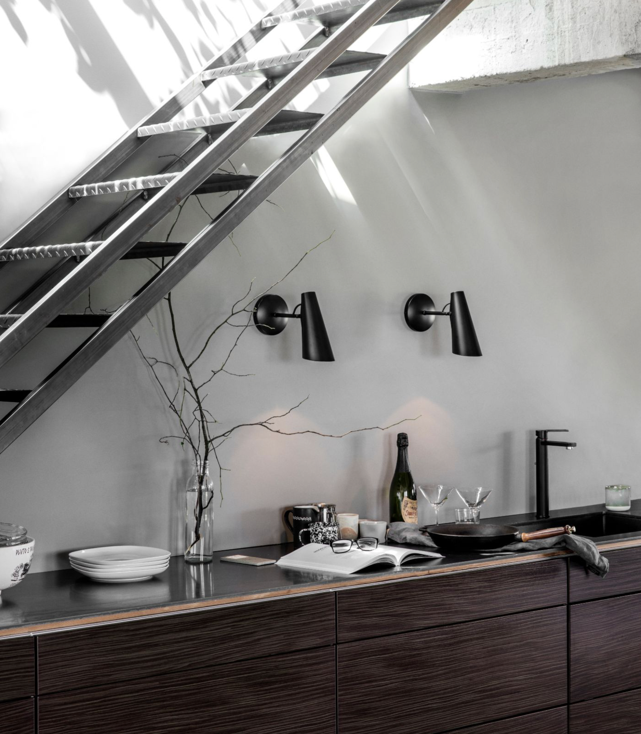 Modern kitchen with dark wood cabinets, black fixtures, and a staircase in the background.