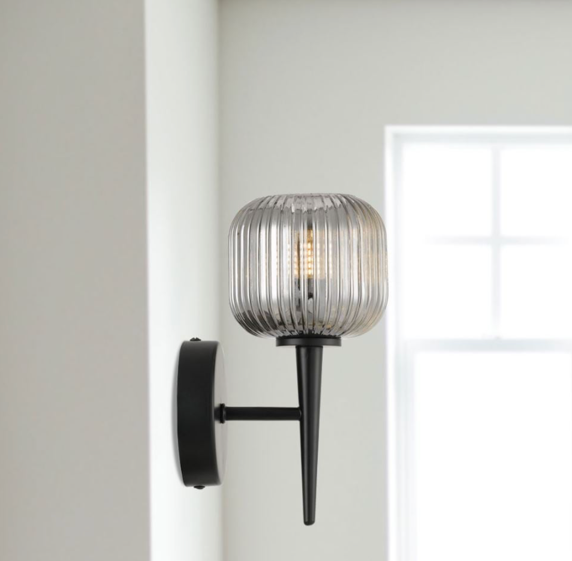 Wall-mounted light fixture with glass shade and black metal arm on a neutral background