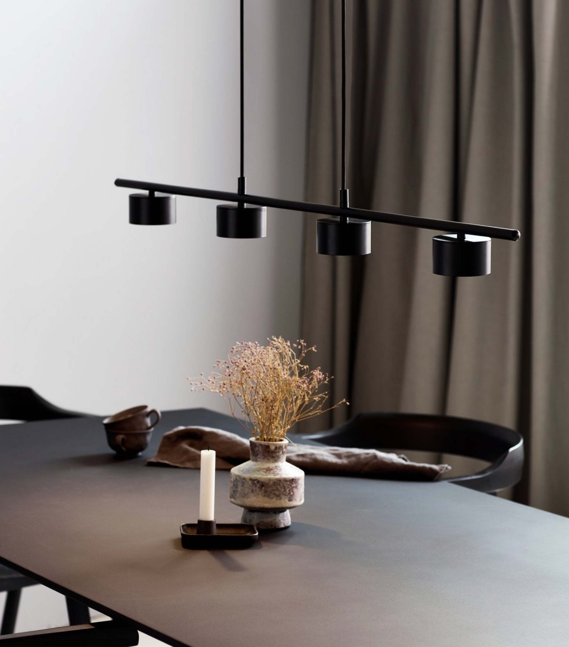 Modern black pendant light fixture over a dining table with decor items.