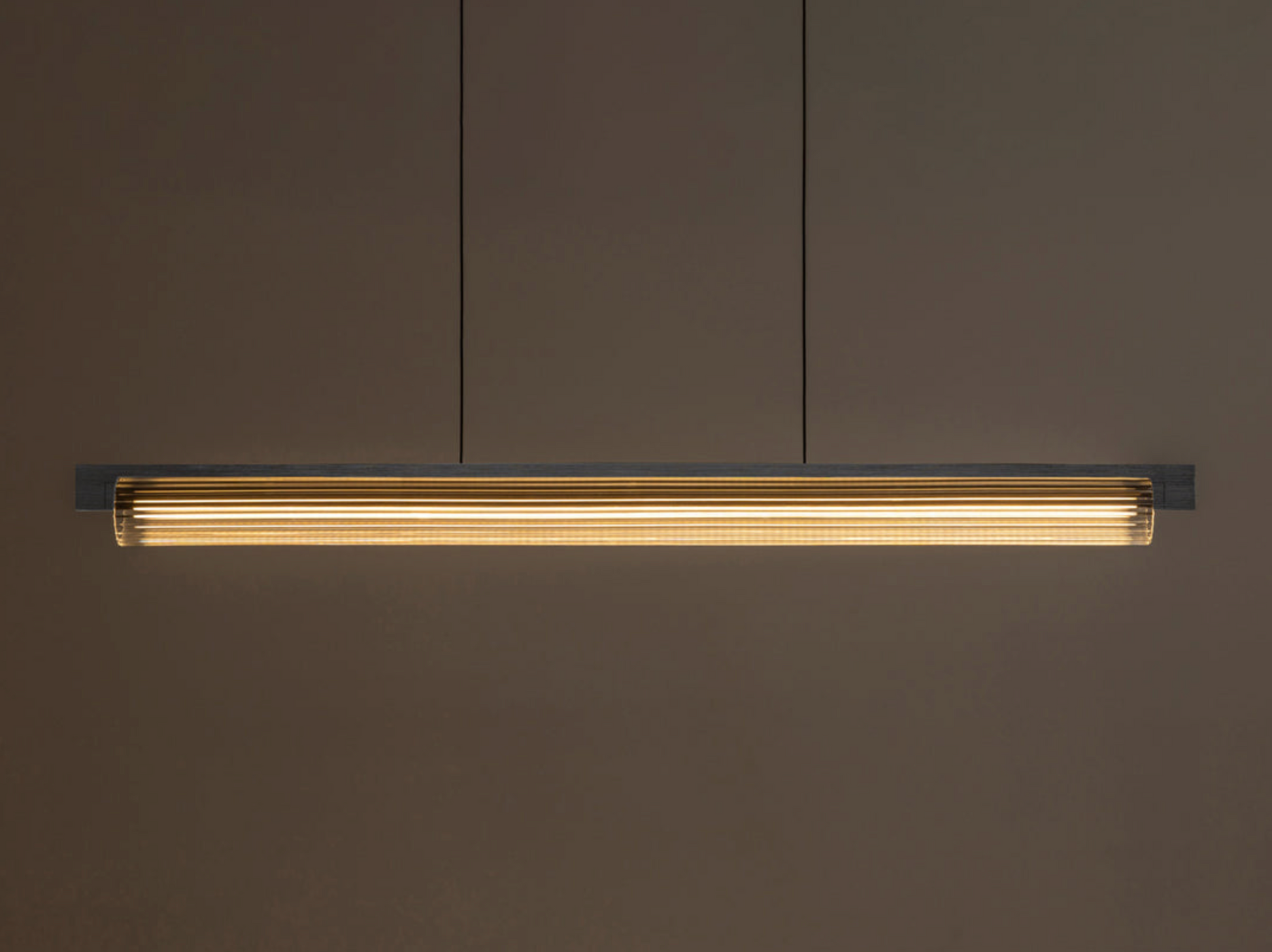 Long linear light fixture with ribbed glass on a dark brown wall