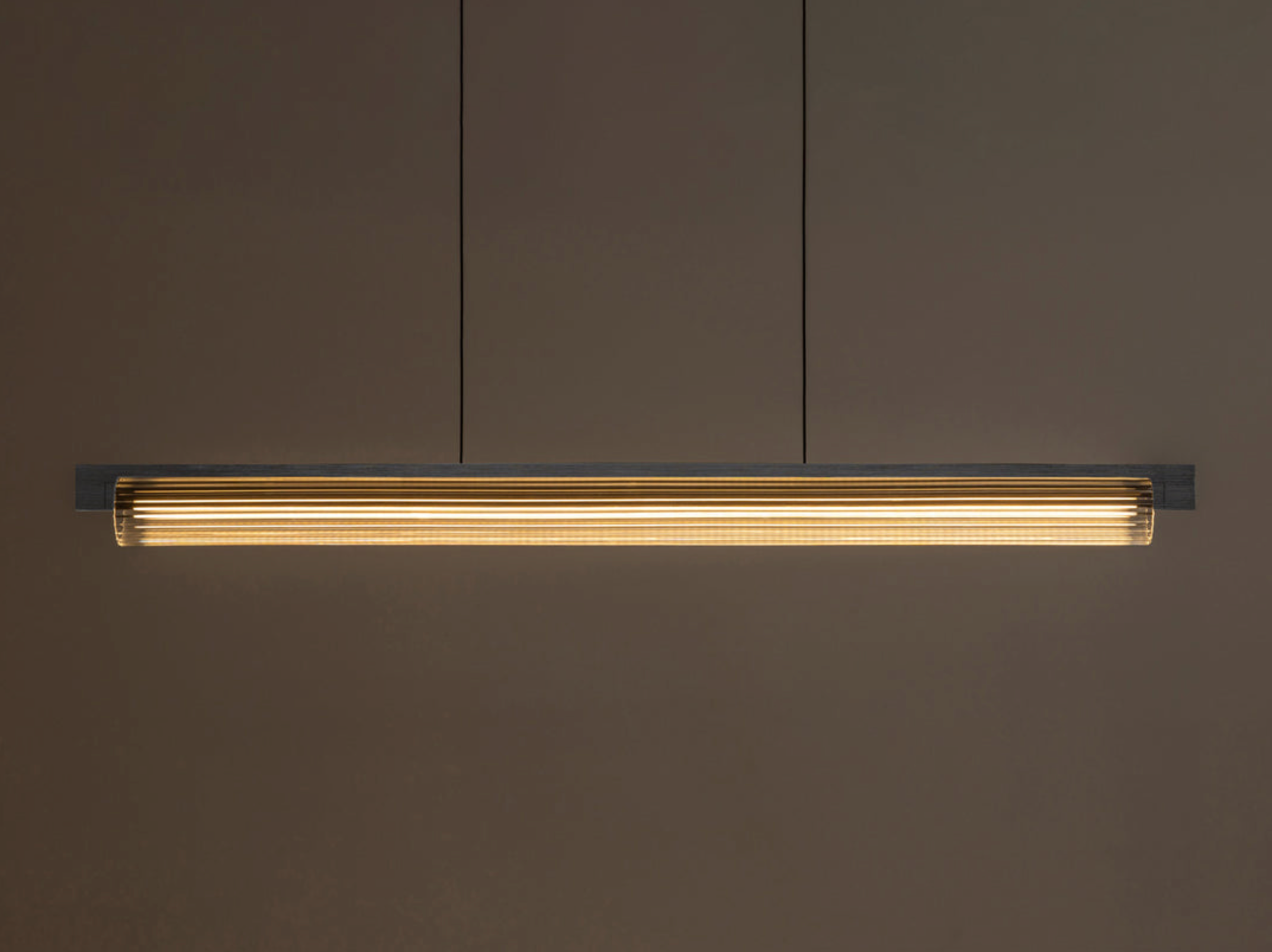 Long linear light fixture with ribbed glass on a dark brown wall