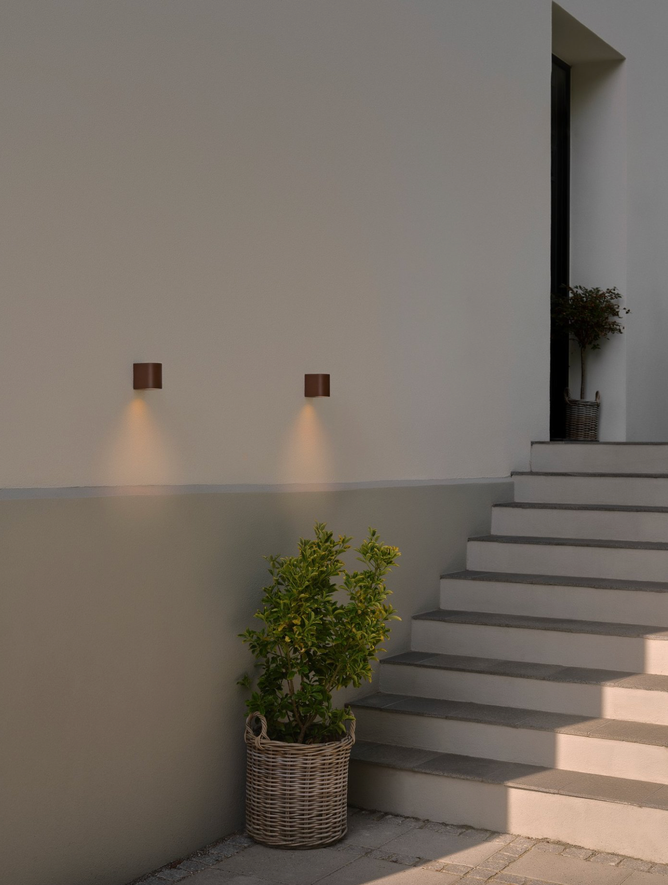 Modern outdoor setting with wall lights, steps, and a plant.