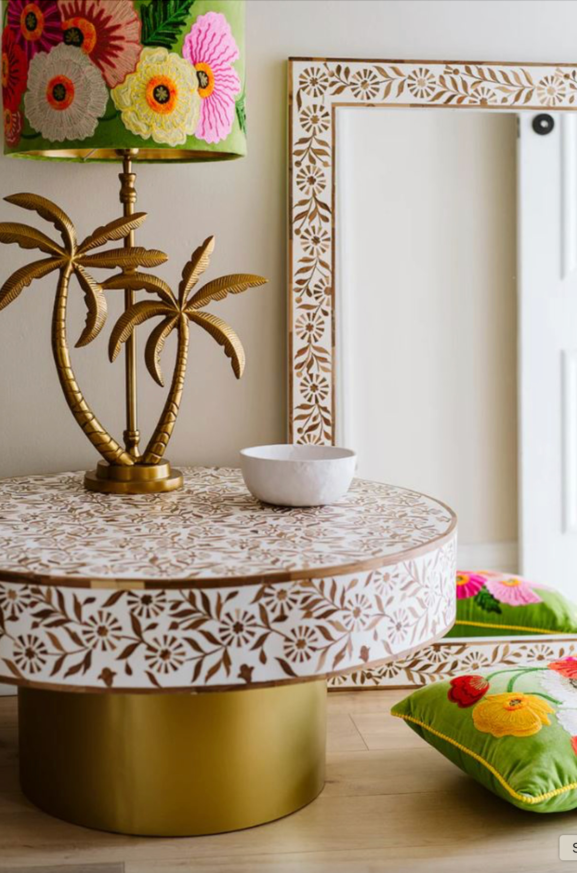 Decorative table with floral patterns, lamp, and cushions in a room setting.