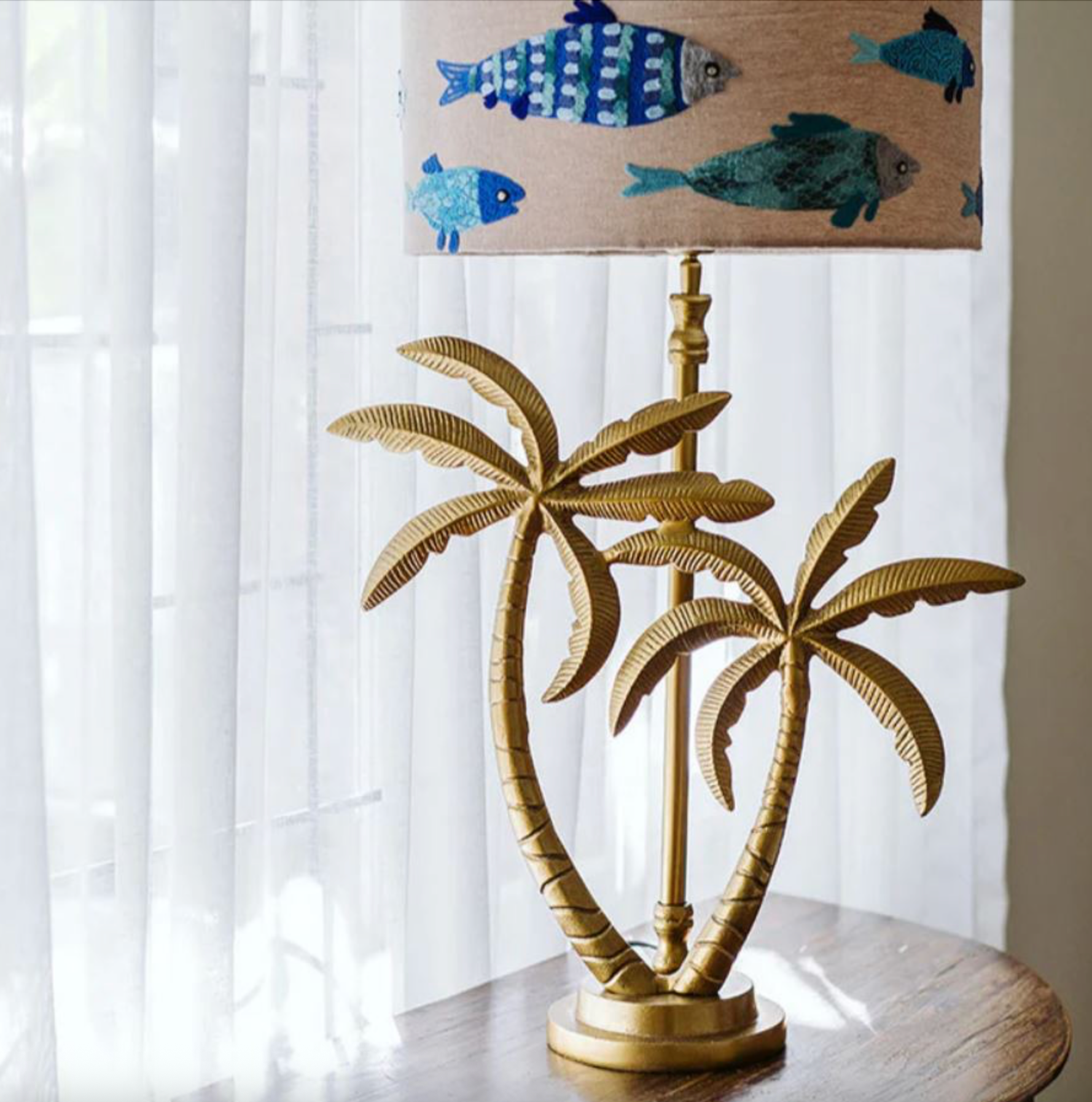 Gold palm tree lamp base with a fish patterned lampshade on a white surface.