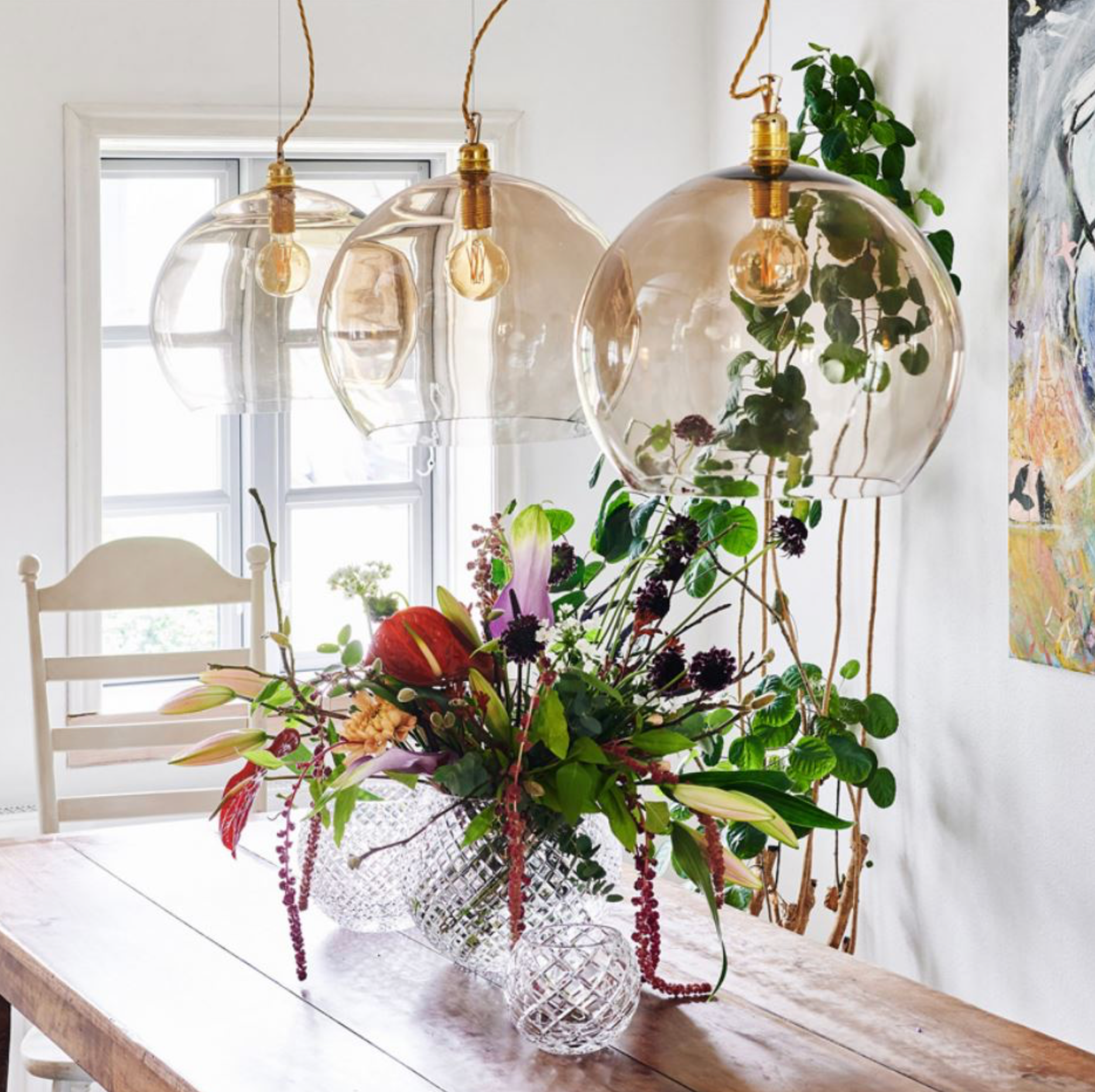 Decorative glass pendant lights with a floral arrangement on a wooden table.