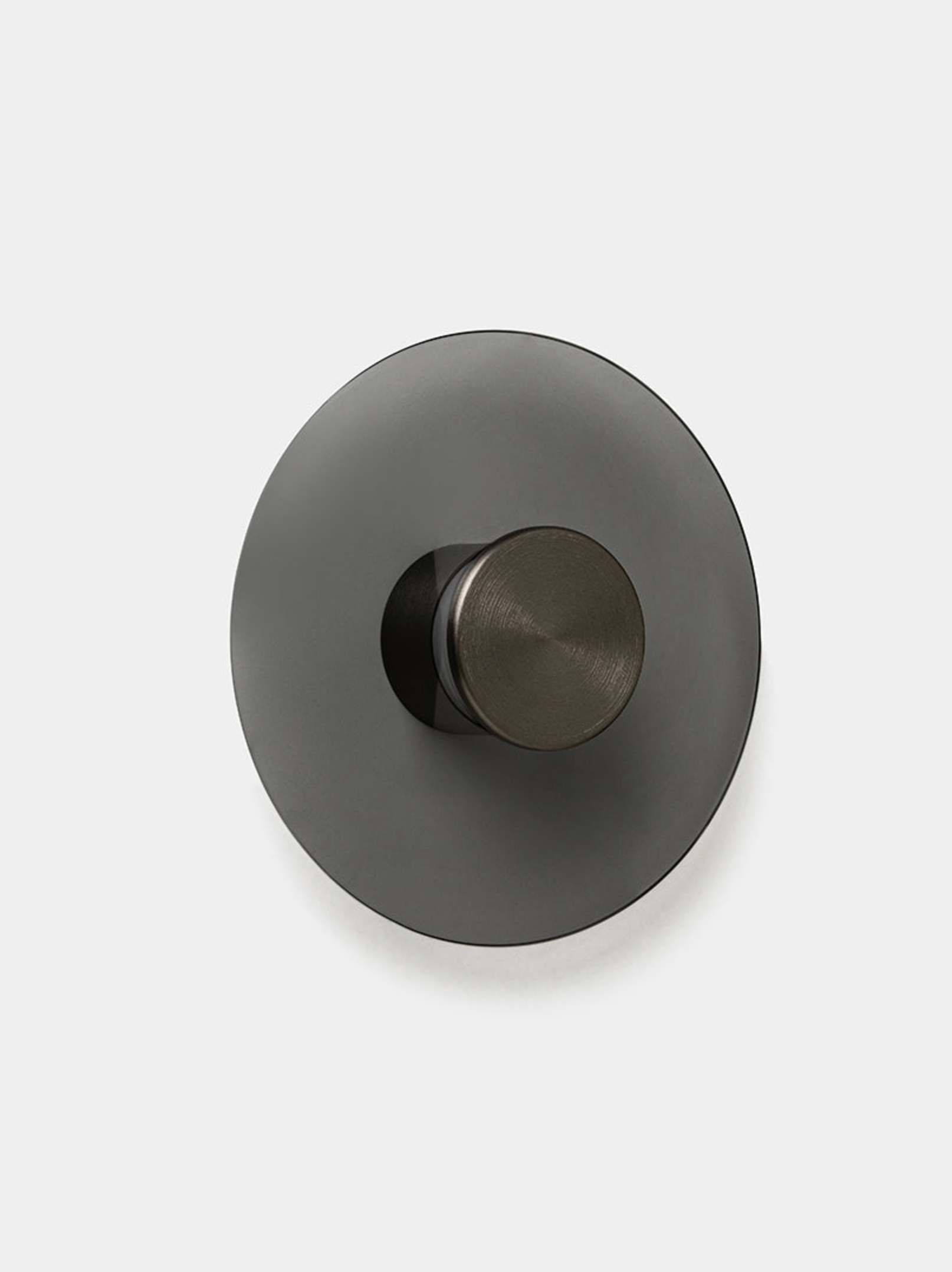 Round metallic wall light with a central knob on a white background