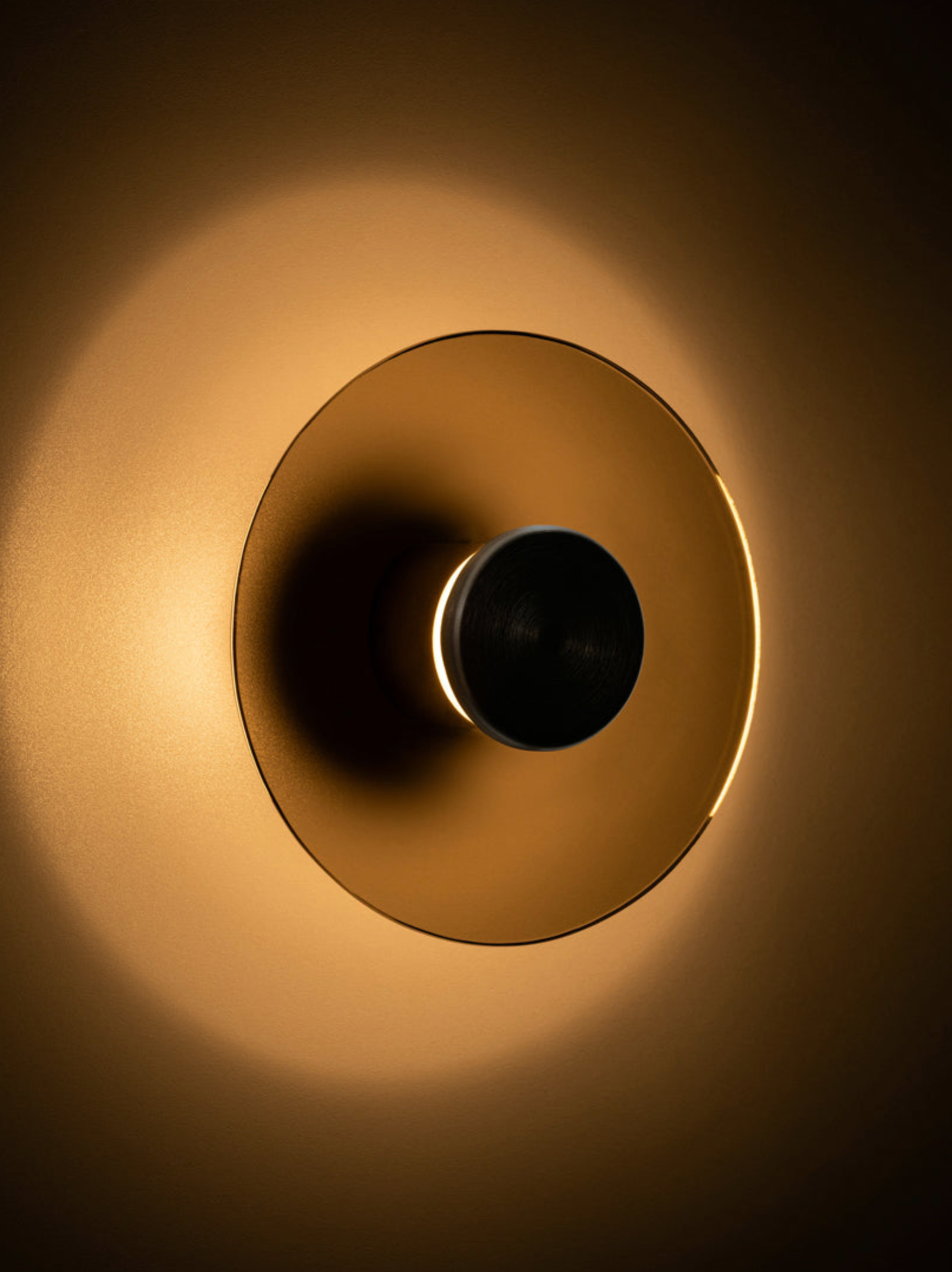 Gold circular wall light with a central black circle on a dark background