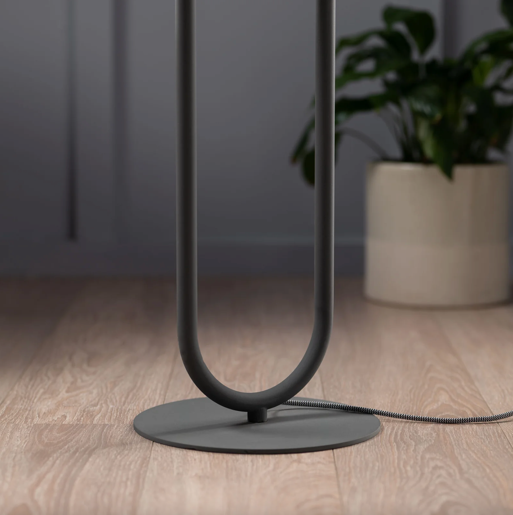 Modern black floor lamp on a wooden floor with a plant in the background