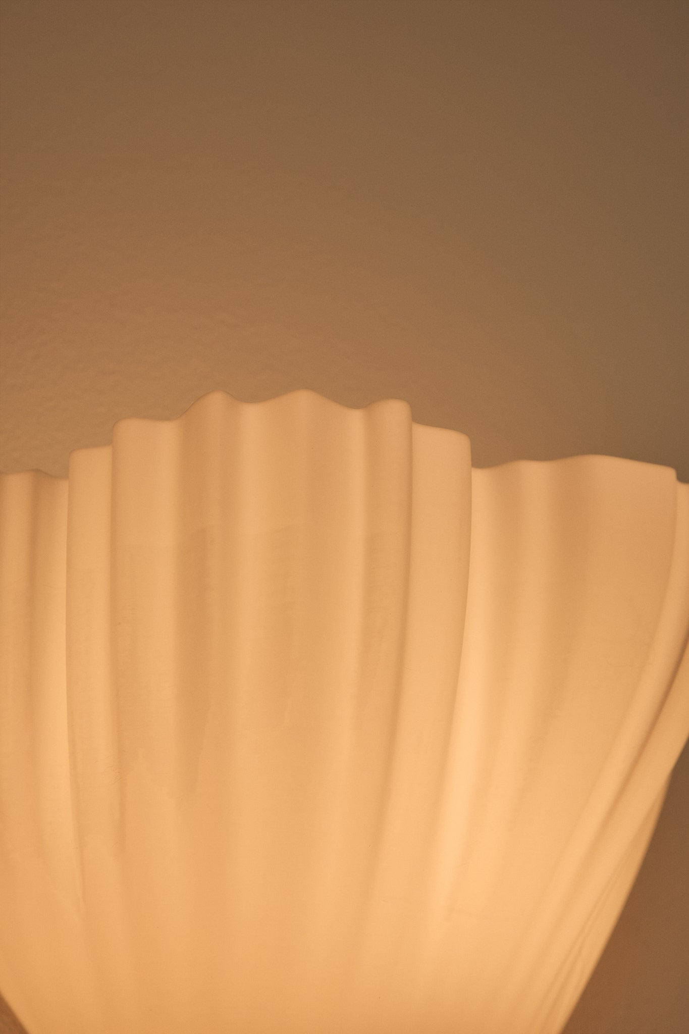 Close-up of a scalloped-edge 3D printed wall lampshade against a beige wall.