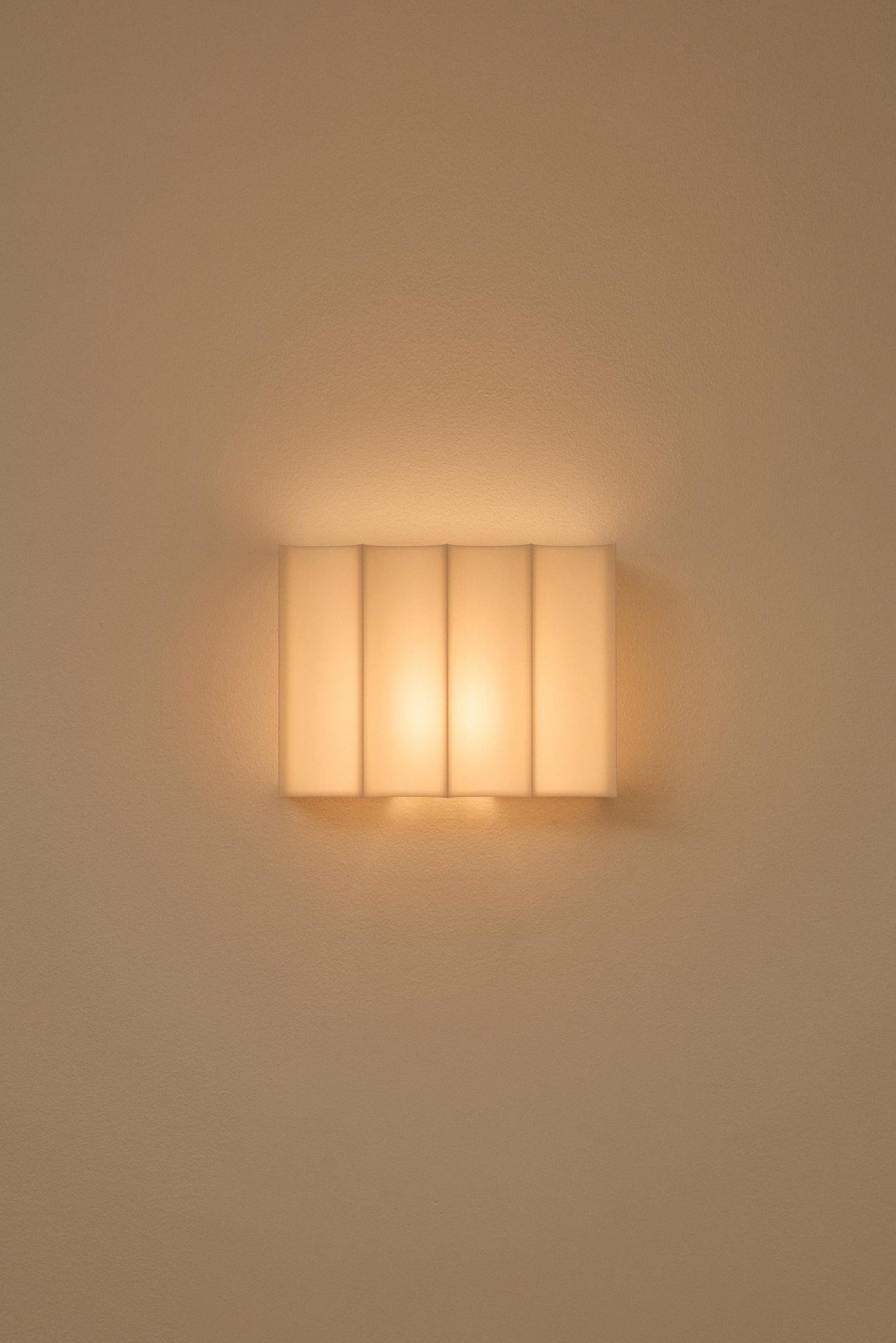 Wall-mounted 3D printed wall light fixture casting a warm glow on a plain wall.