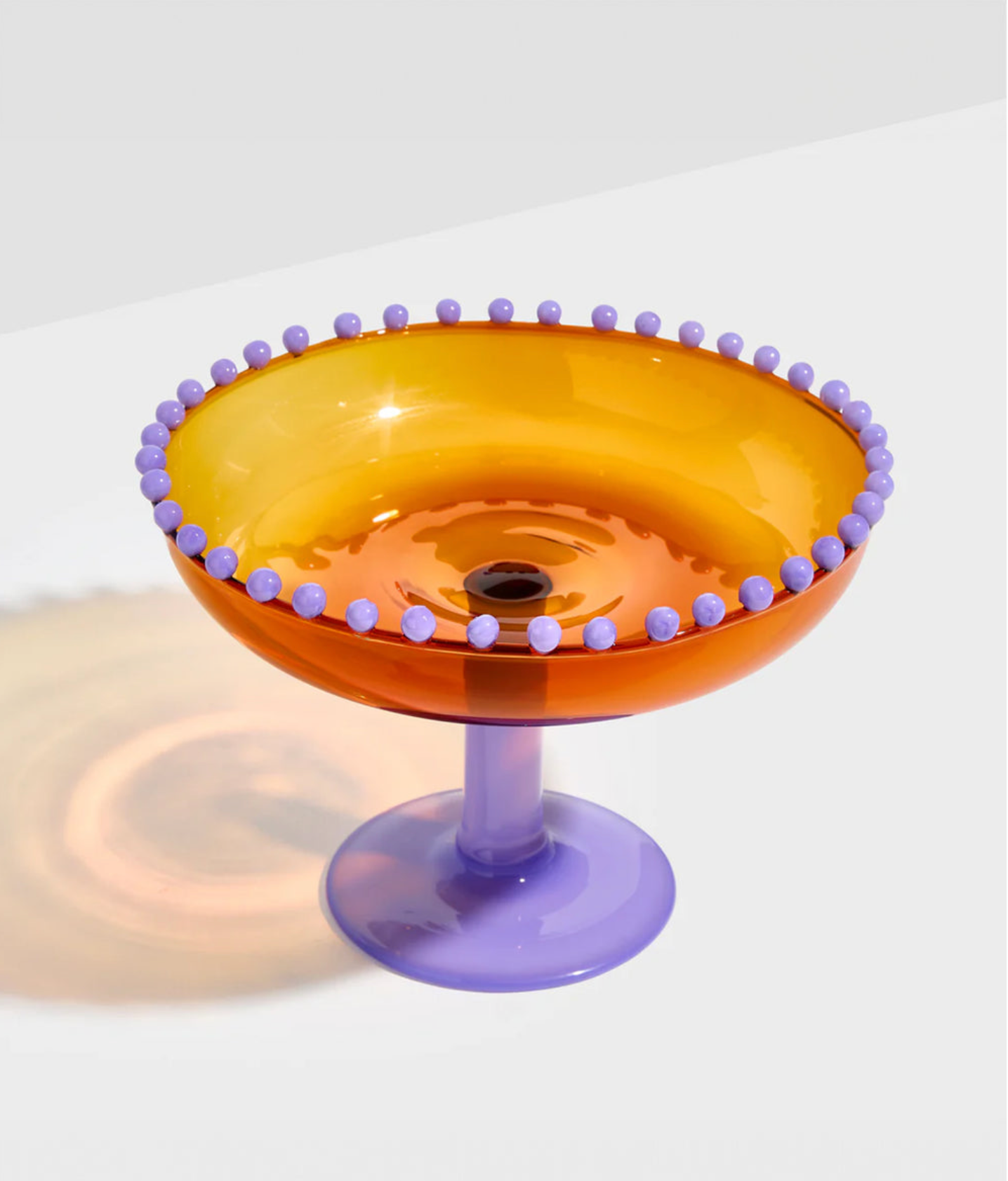 Orange glass bowl with purple rim and base on a white background