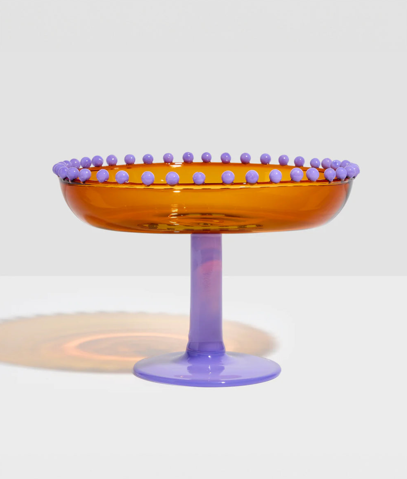 Transparent amber glass coupe with purple rim and base on a white background