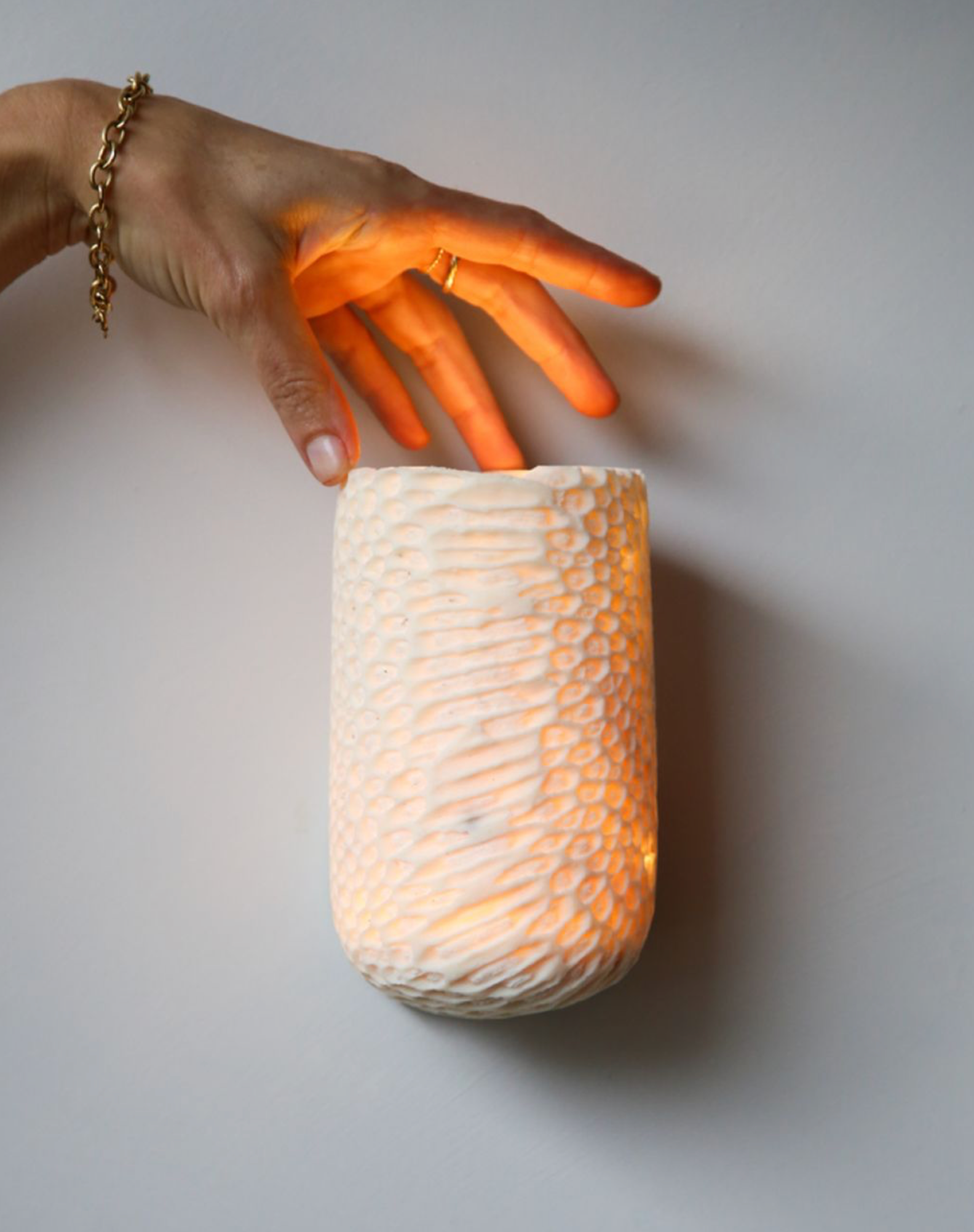 Hand holding a textured fossil wall light against a plain background