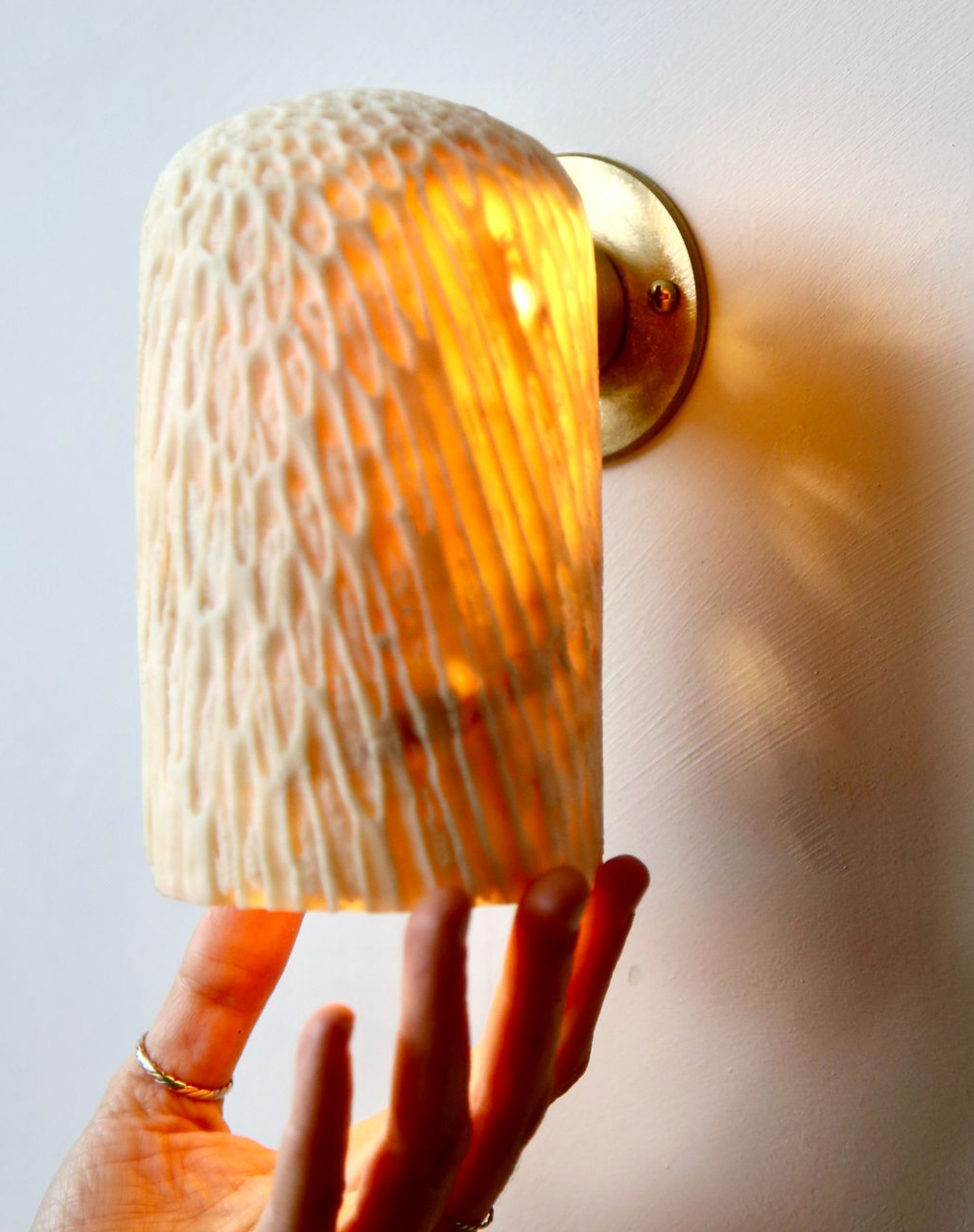 Wall-mounted lamp with textured glass shade held by a hand against a light background
