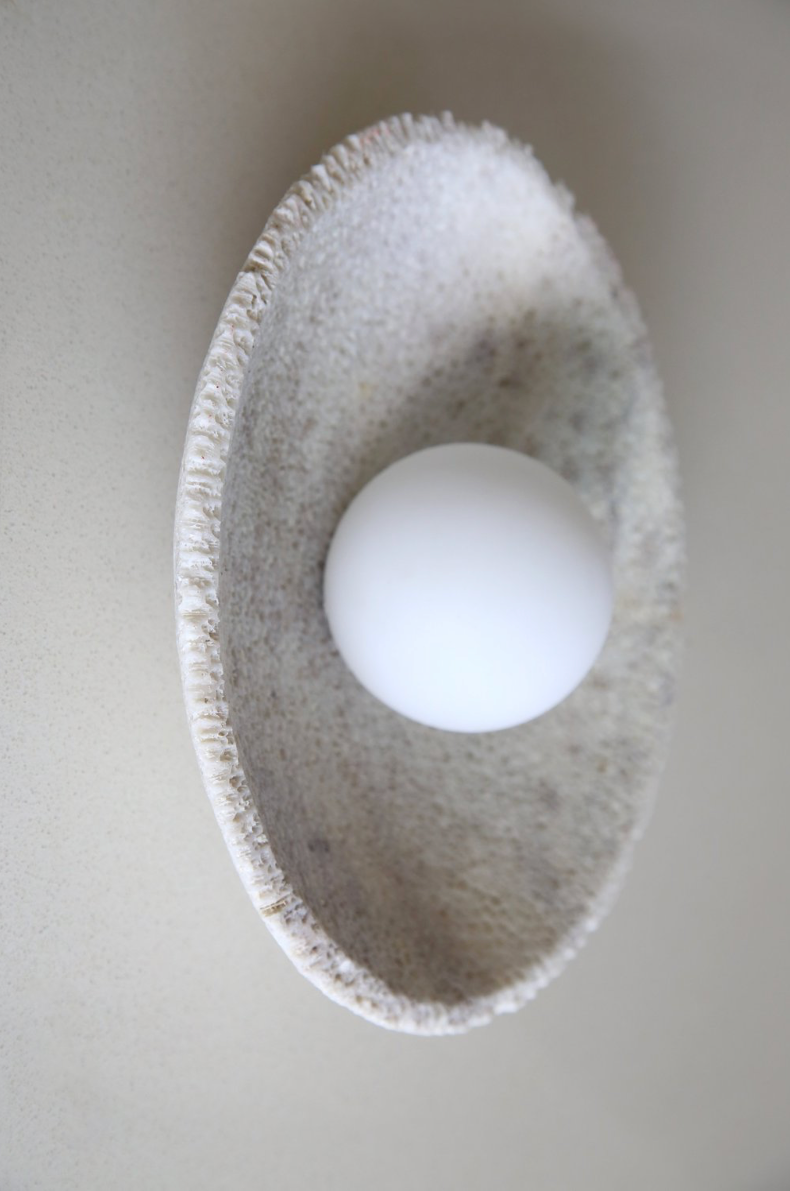 White ball inside a textured coral grey wall sconce on a light grey background