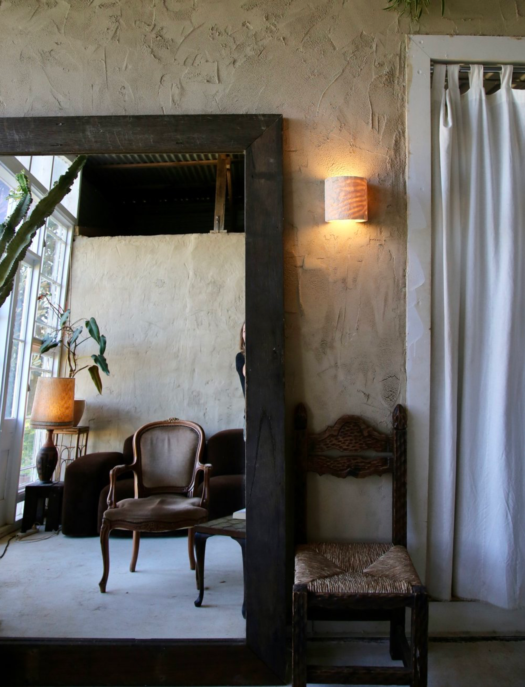 Room with a large mirror reflecting a chair and a light fixture on the wall.