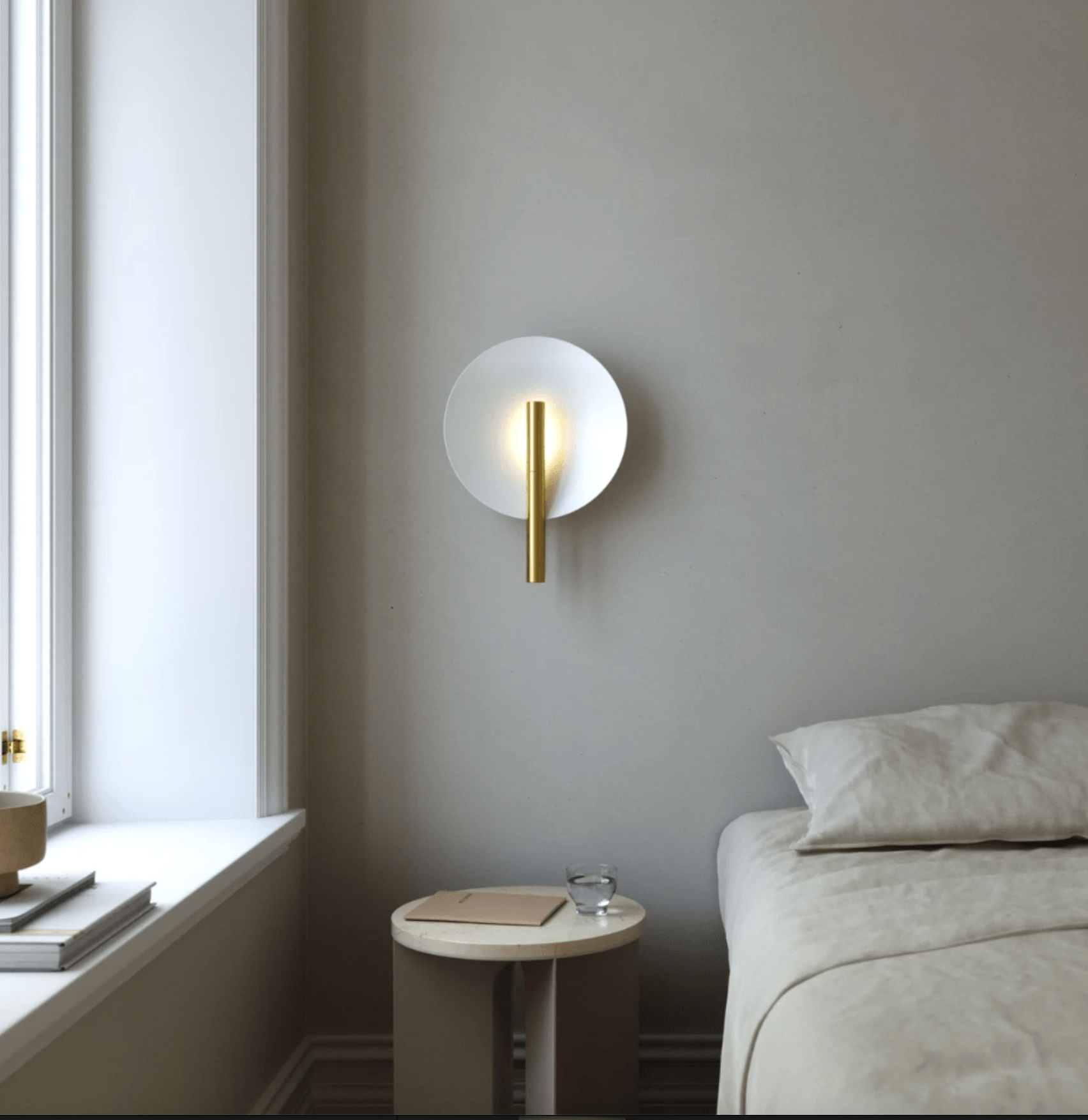 Modern wall sconce in a bedroom setting with a bed and window.