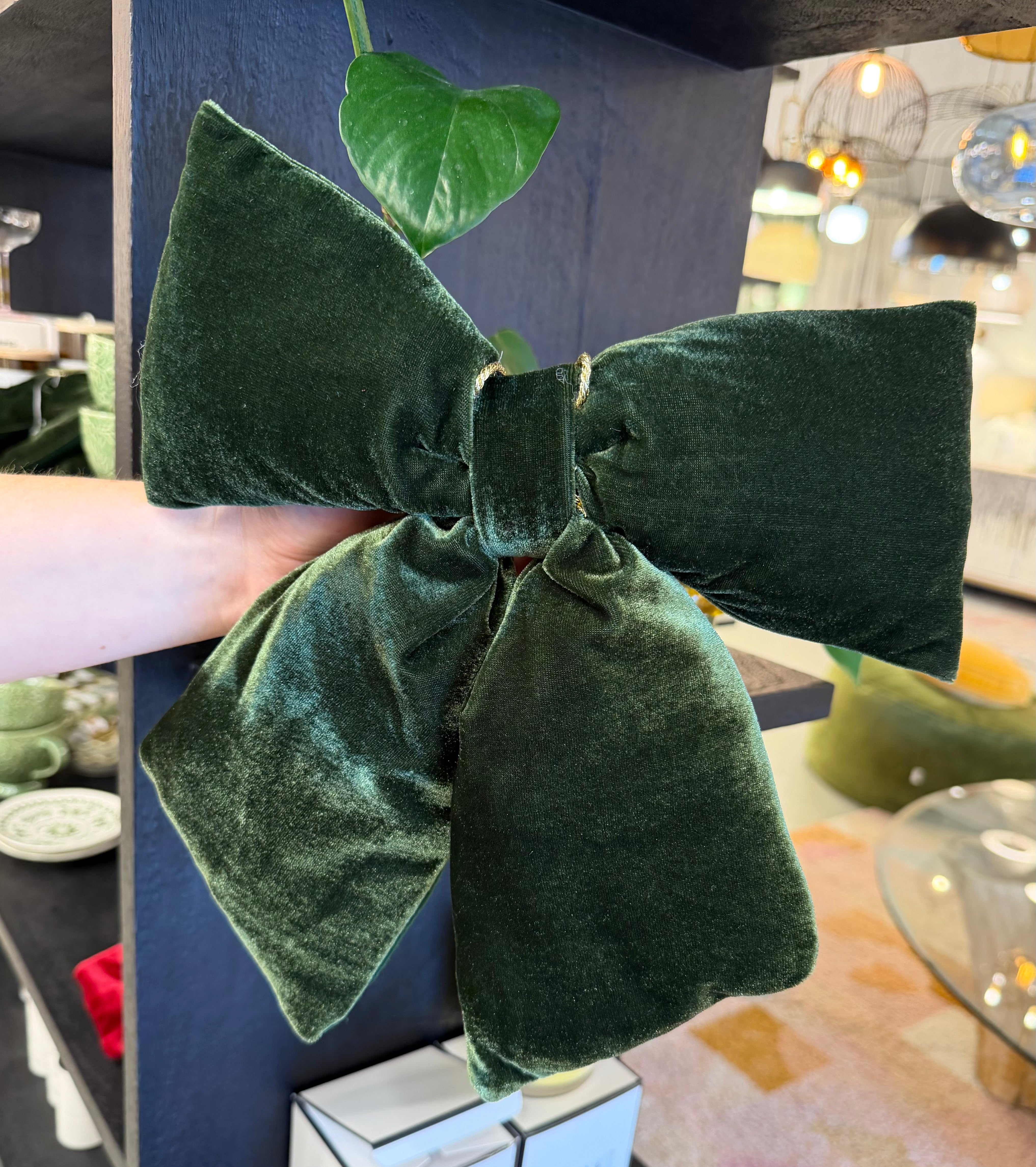 Green velvet bow held by a hand against a blurred indoor background