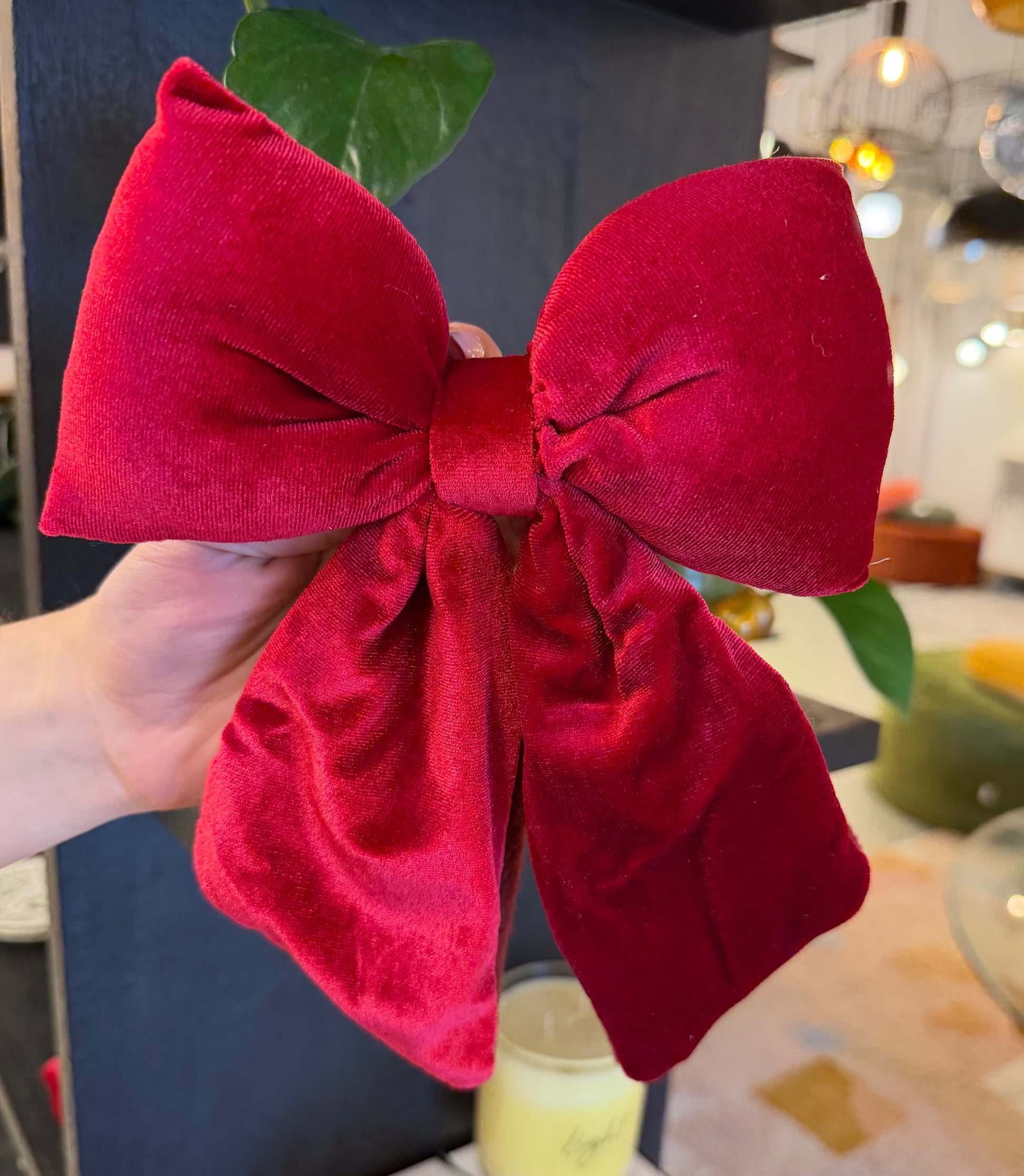 Red velvet bow held by a hand with a blurred indoor background