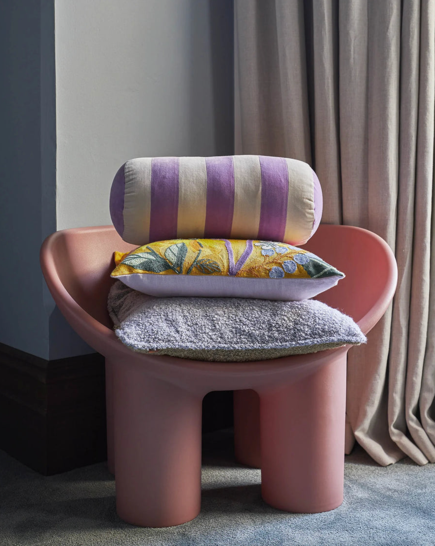 Pink chair with colorful cushions against a neutral background