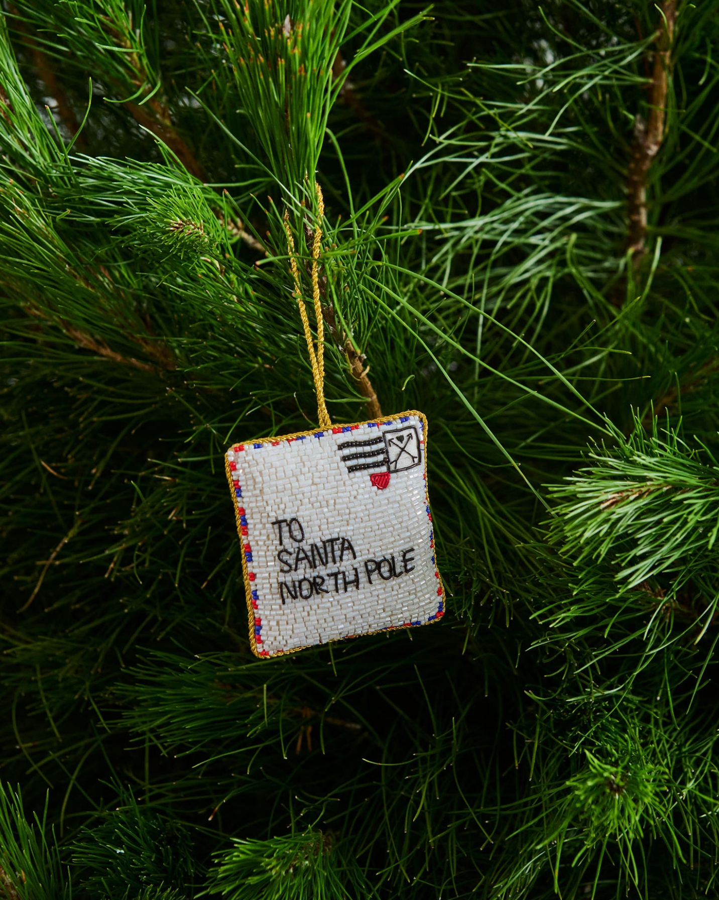 Decorative ornament with beaded 'To Santa North Pole' text hanging on a Christmas tree.