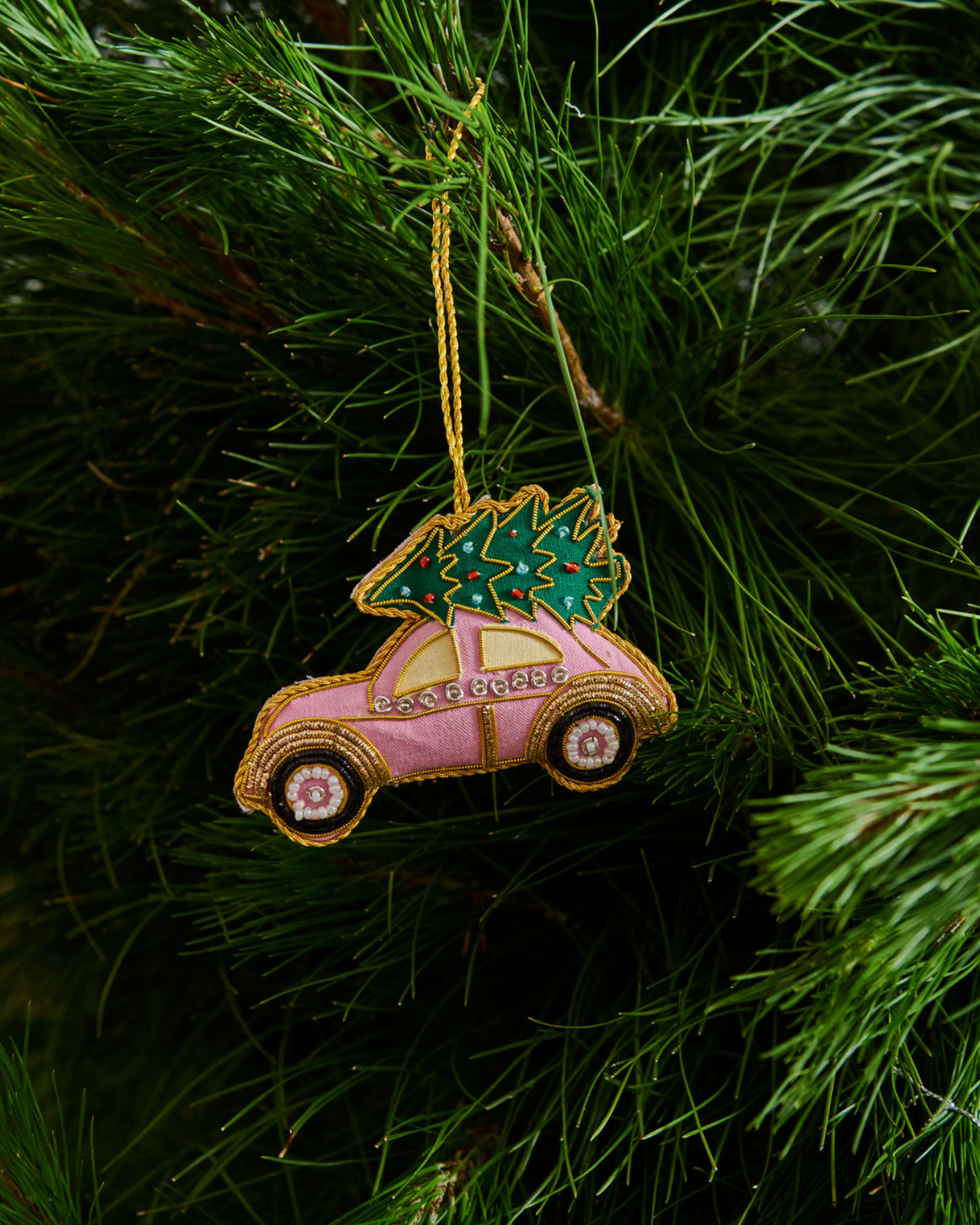 Decorative ornament shaped like a pink car with a green tree on a Christmas tree.